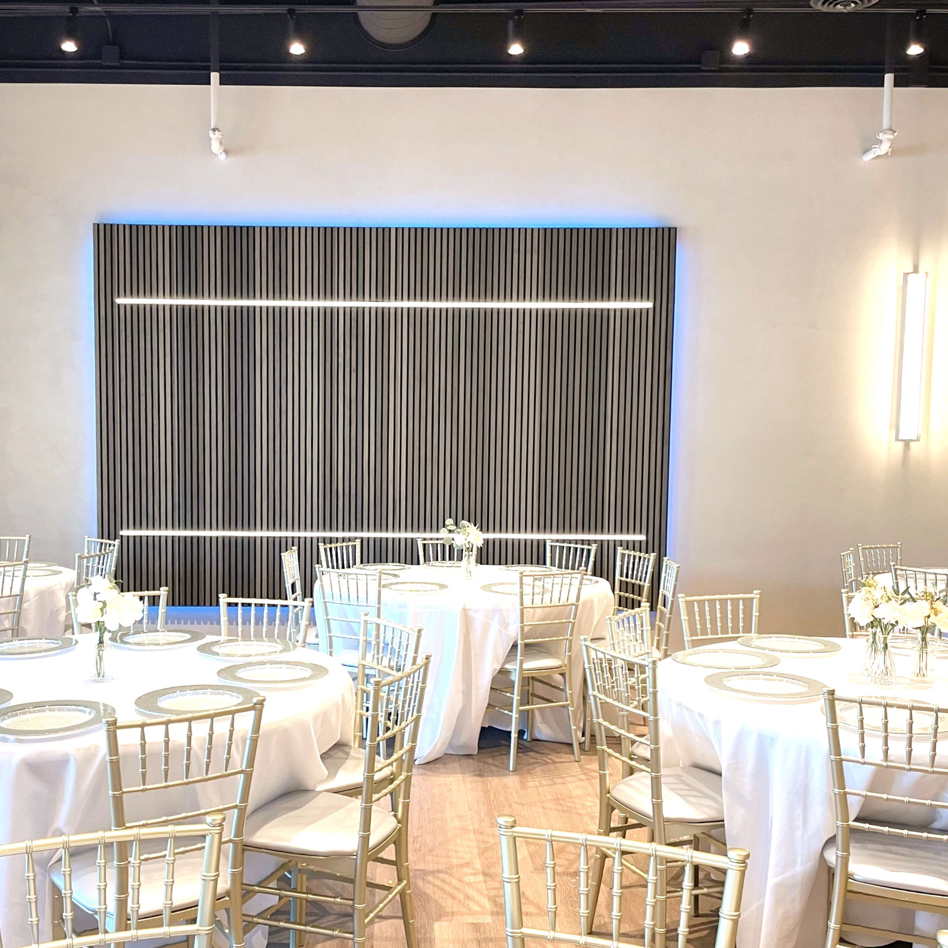 A banquet hall set with round tables, each dressed in white tablecloths and adorned with floral centerpieces, under modern lighting.