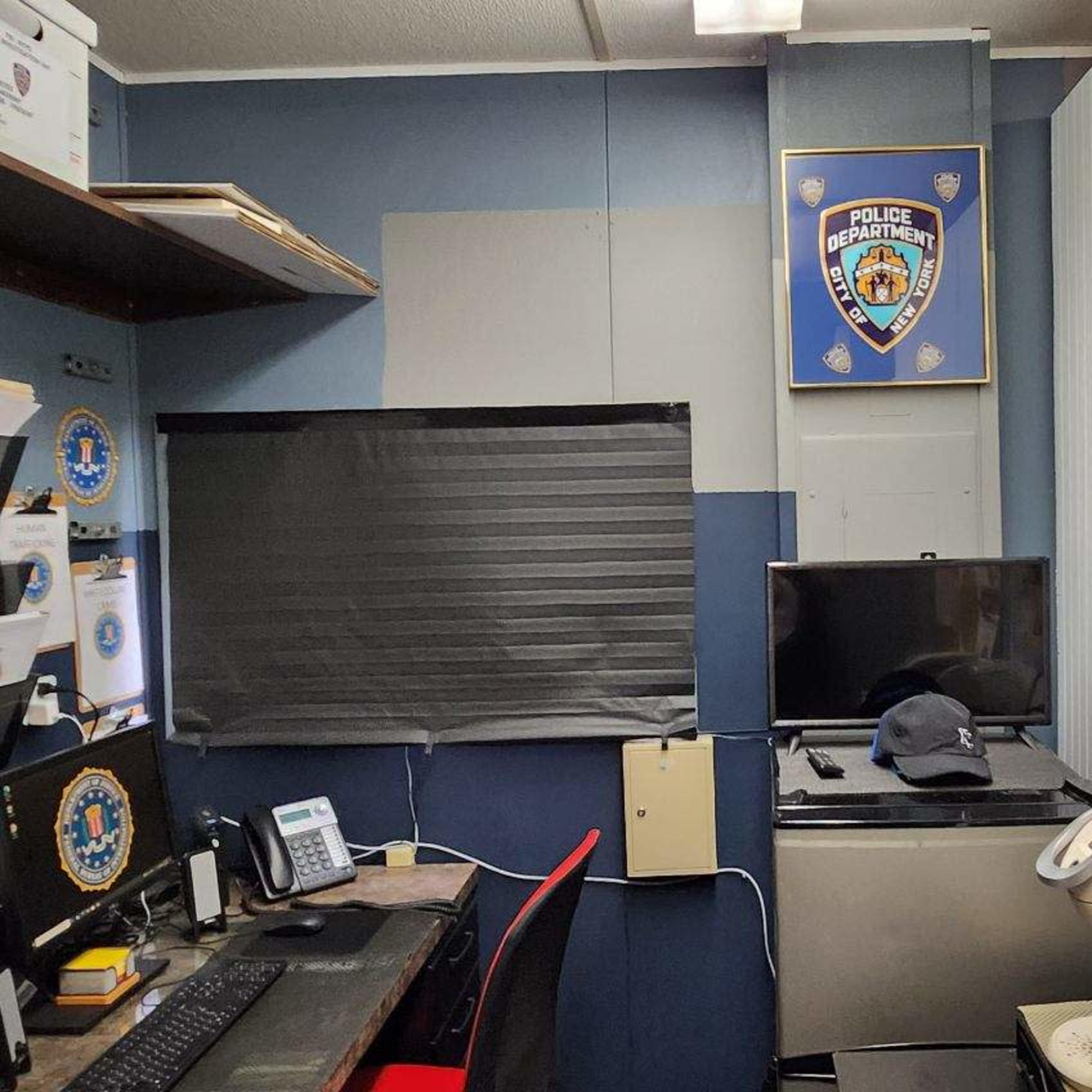 A small office space with a desk, computer, and various police department insignias on the walls.