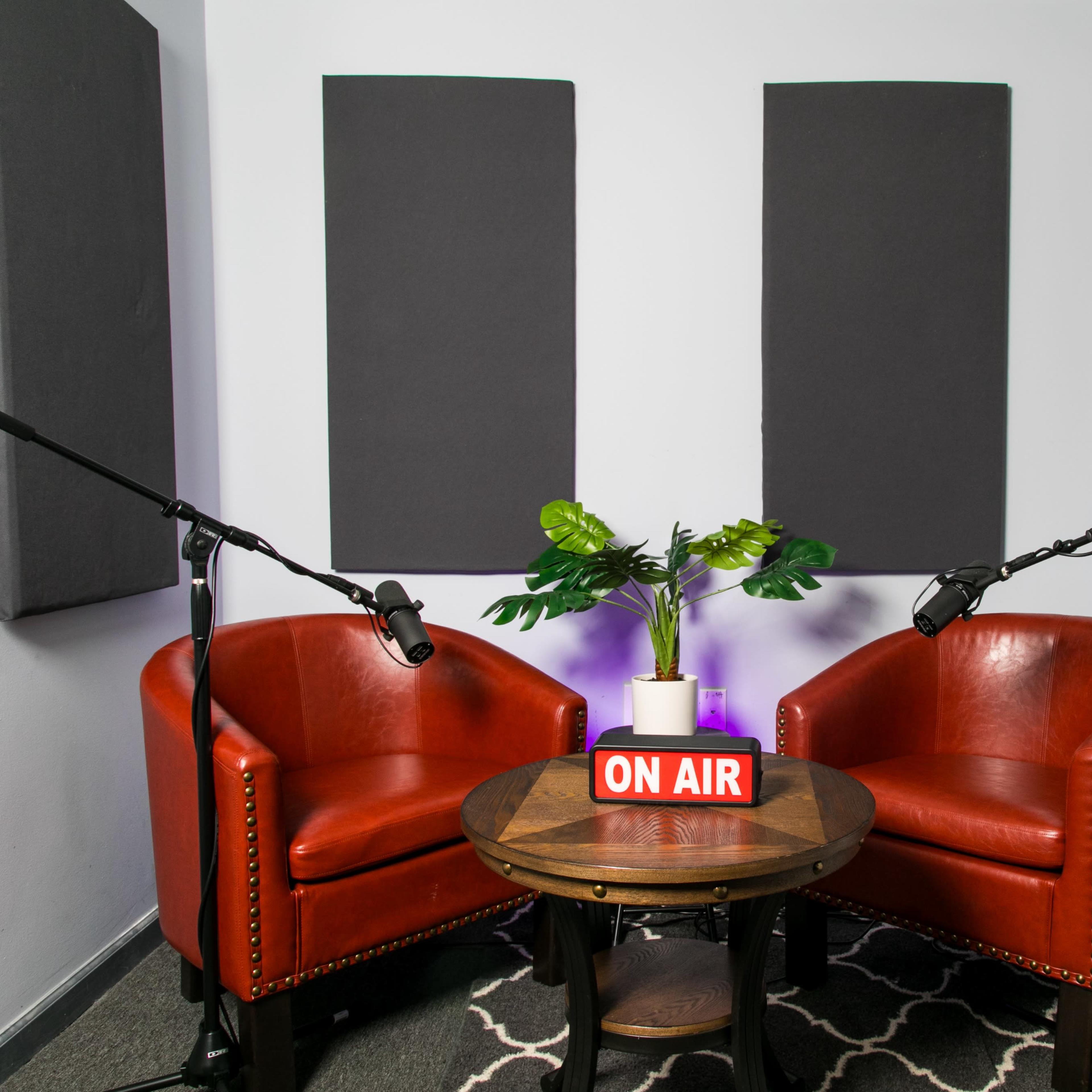 A small recording studio setup with two red chairs facing each other, a round table with a "ON AIR" sign, and microphones positioned on either side.
