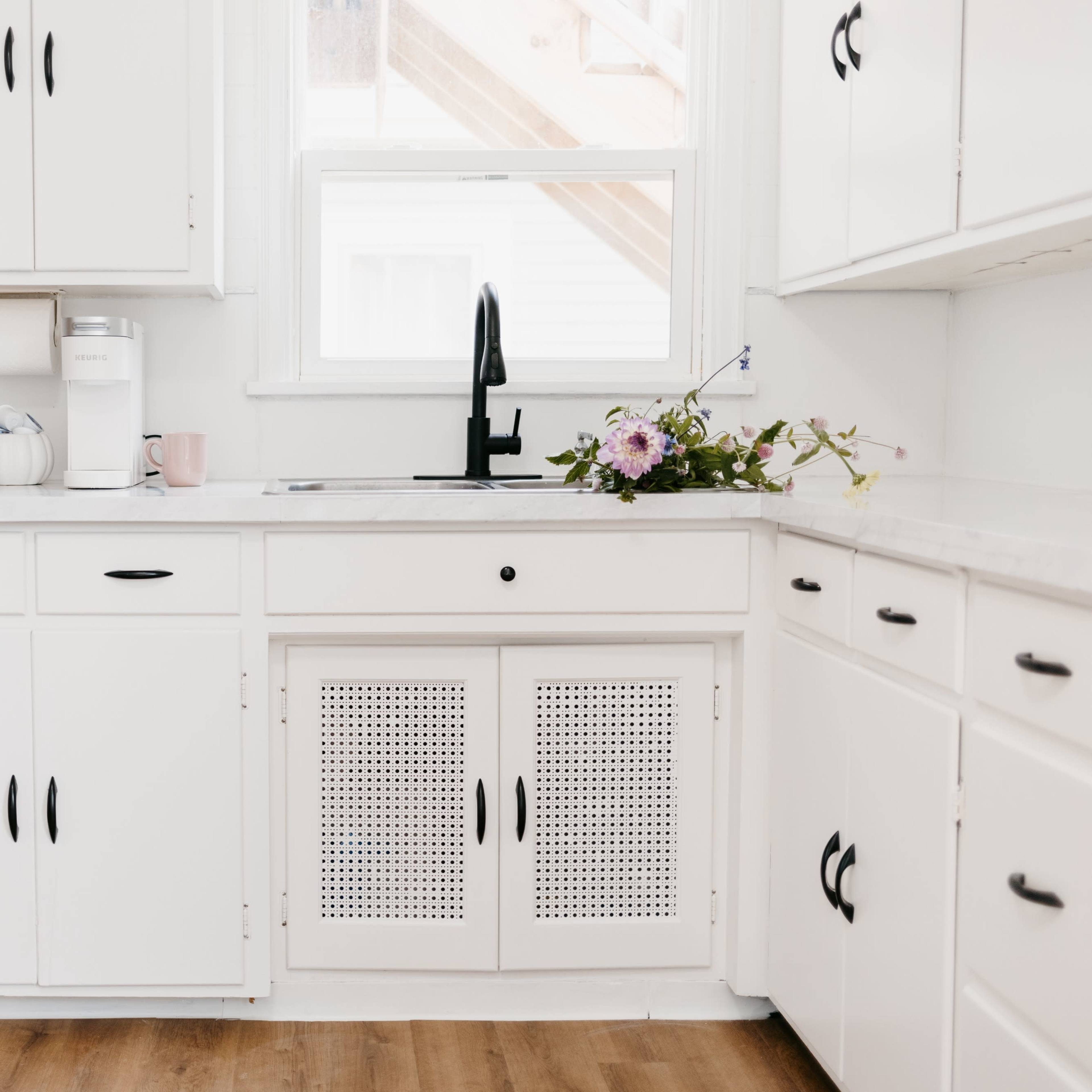 A minimalist kitchen features white cabinets, a sink with a black faucet, and a small vase of flowers on the countertop.