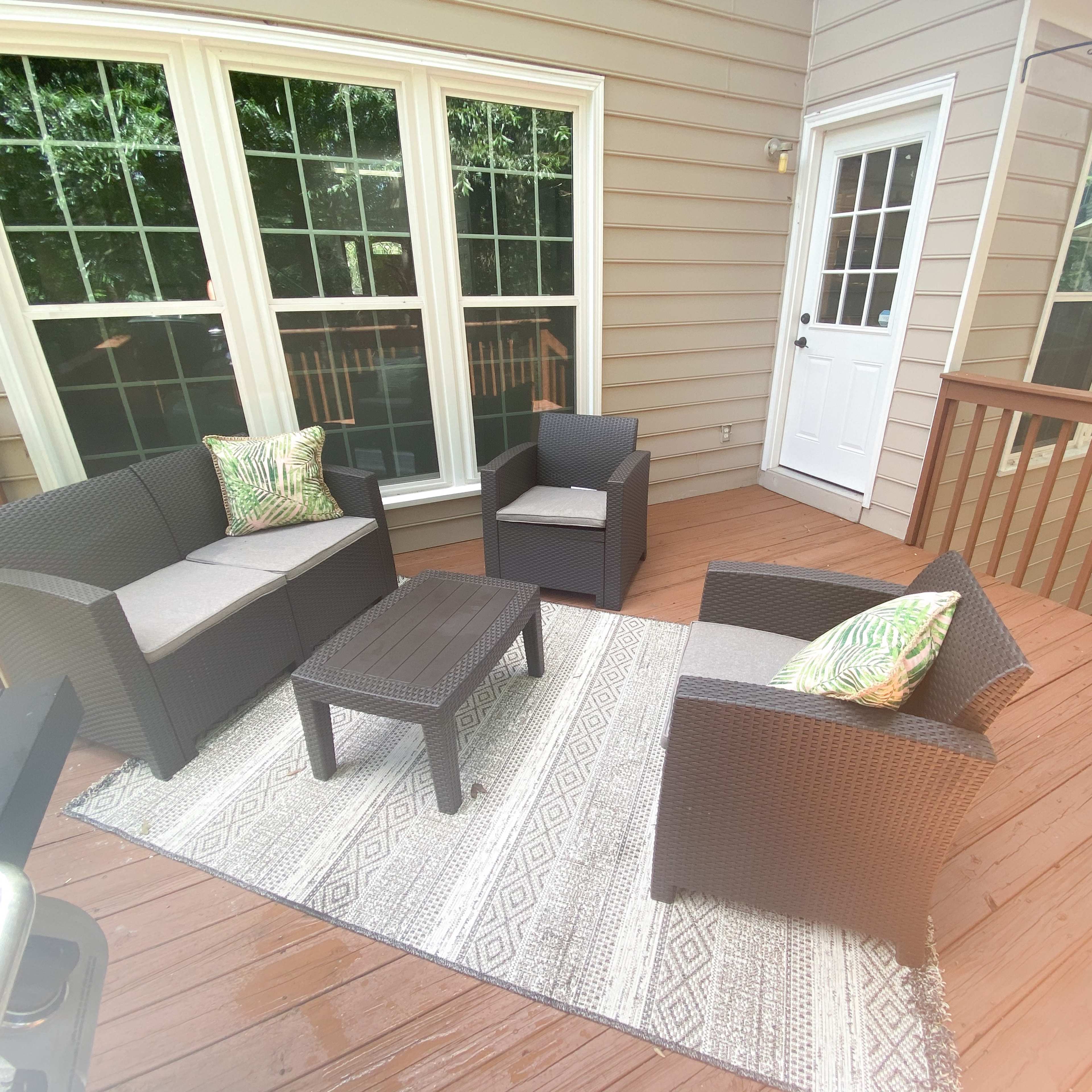 A patio features a seating arrangement with wicker furniture and a patterned rug, alongside a door leading outside.