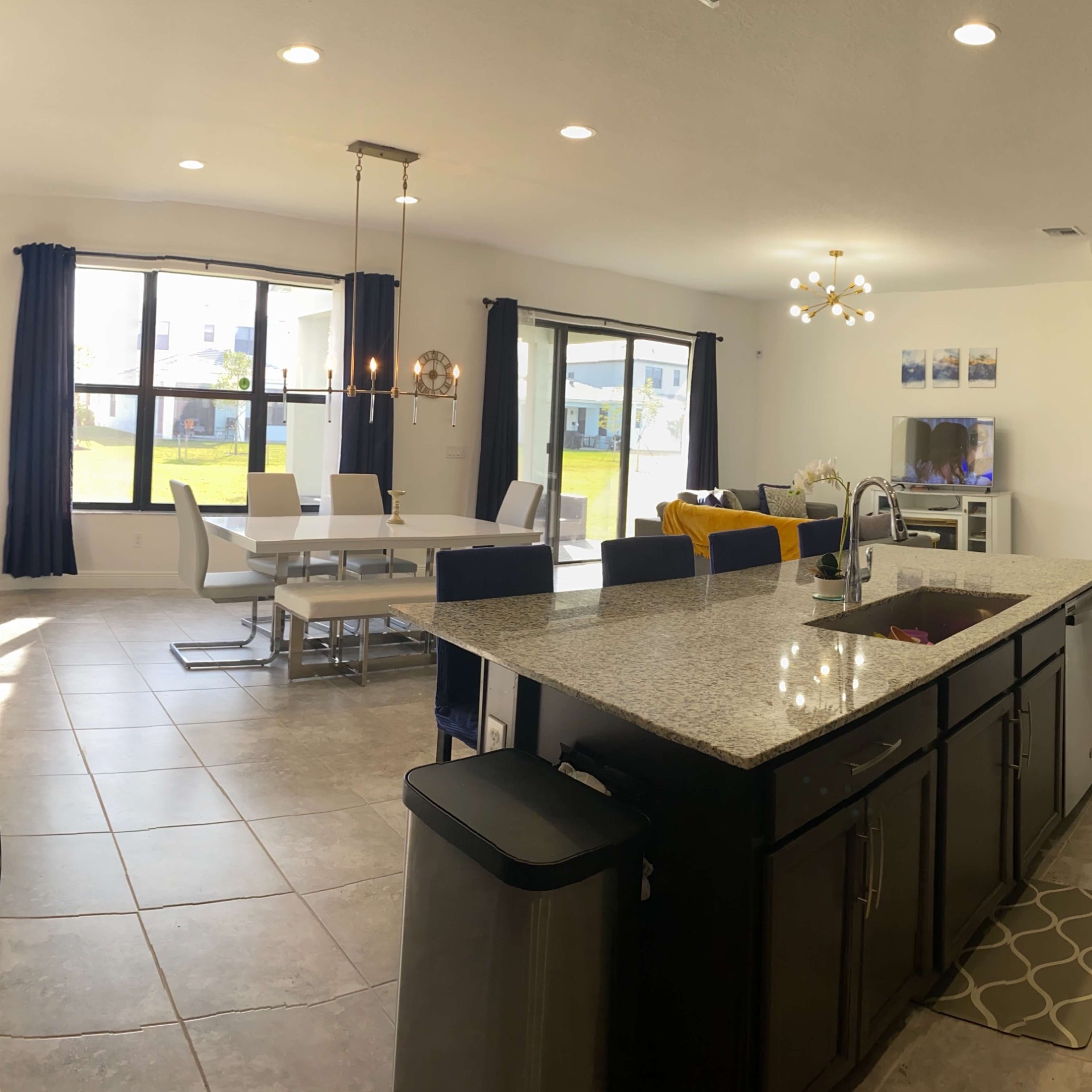 A modern kitchen with granite countertops opens to a dining area and living room, featuring large windows that provide natural light.