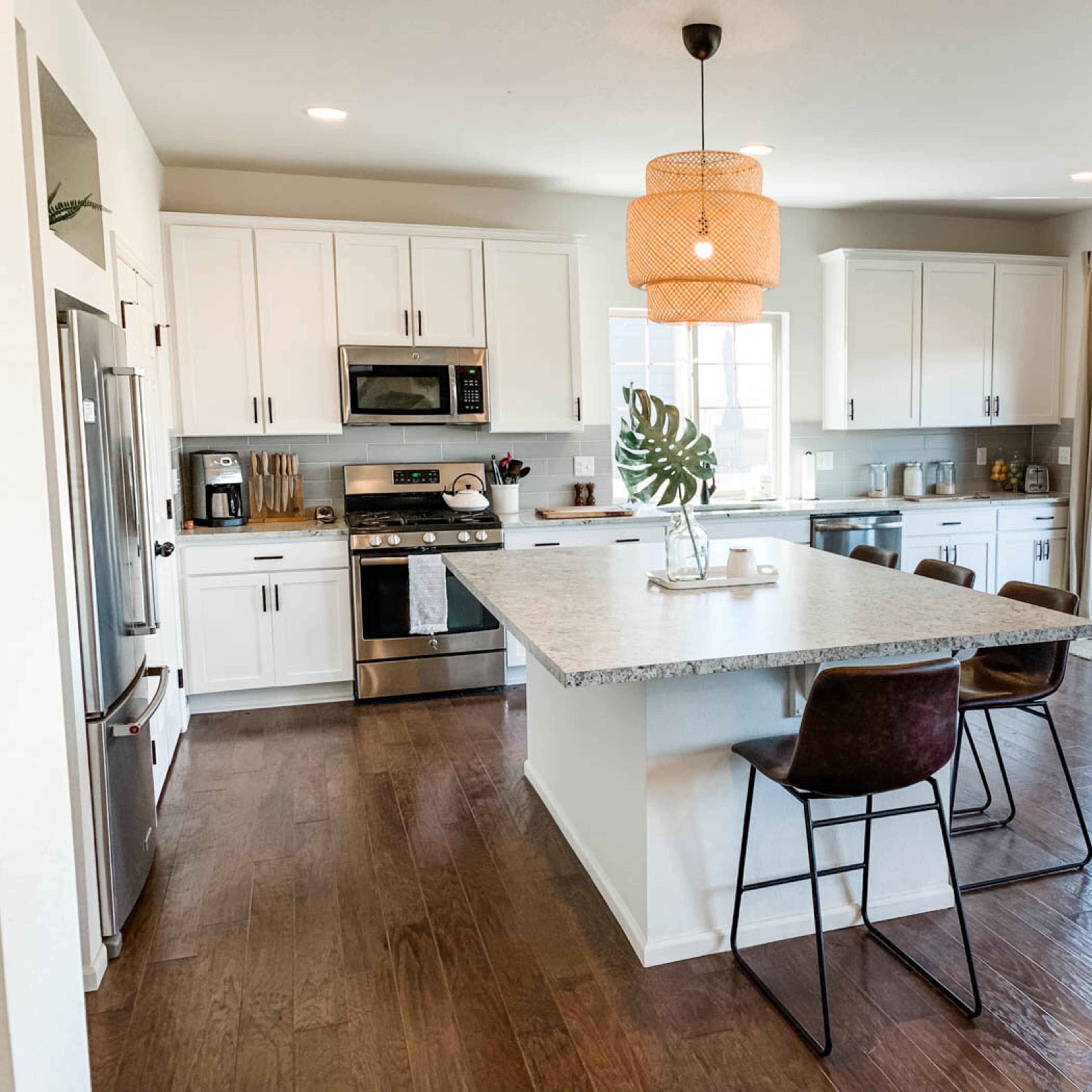 A modern kitchen features white cabinetry, stainless steel appliances, a large island with seating, and a sliding glass door leading to an outdoor area.