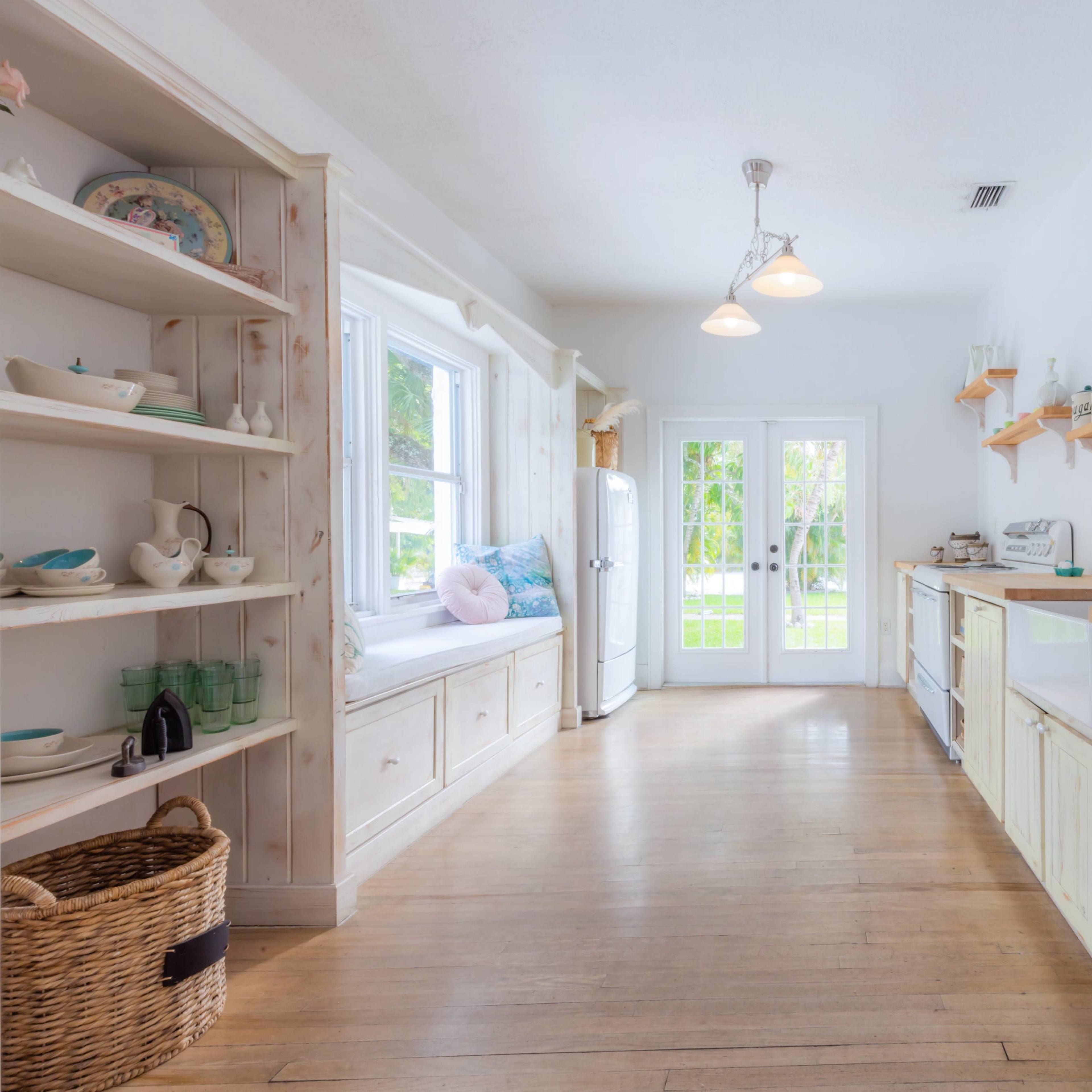 A bright kitchen with white cabinetry, wooden countertops, and large windows overlooking a patio area.