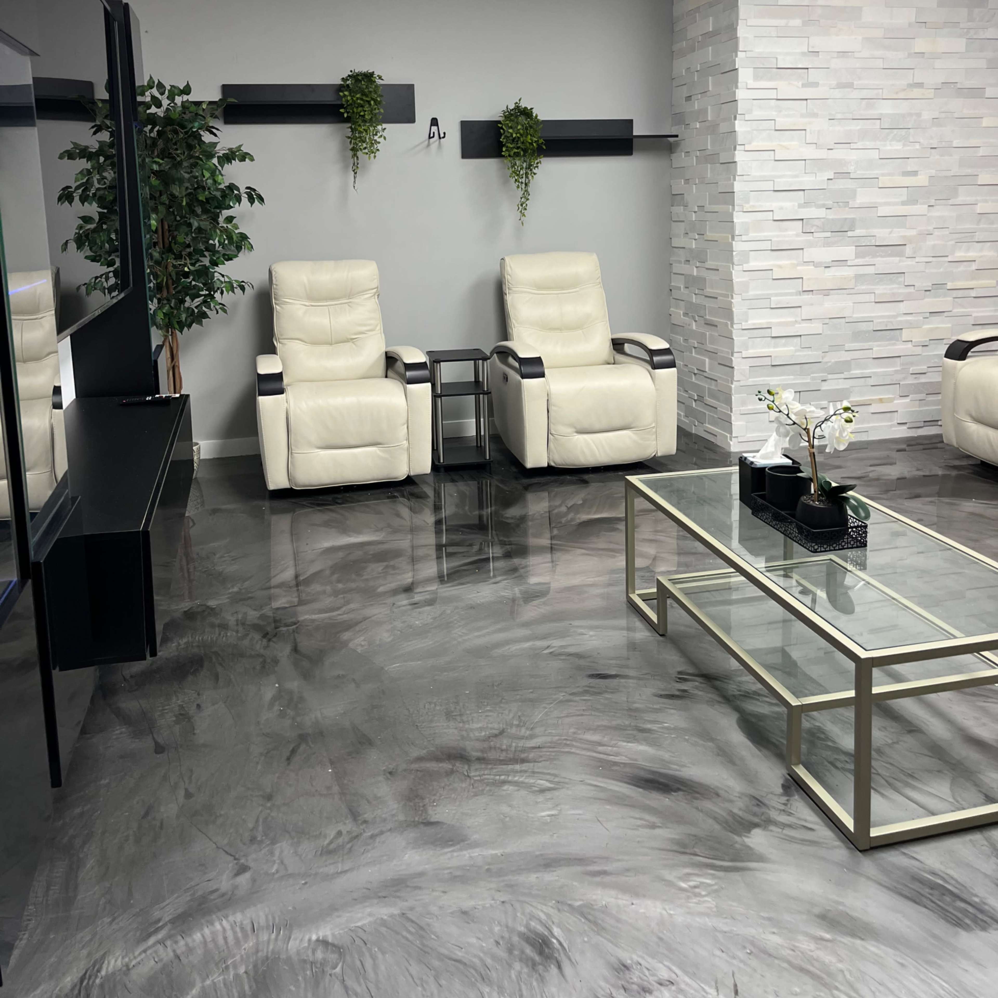 A modern waiting room with two white reclining chairs, a glass coffee table, and a textured gray stone wall.