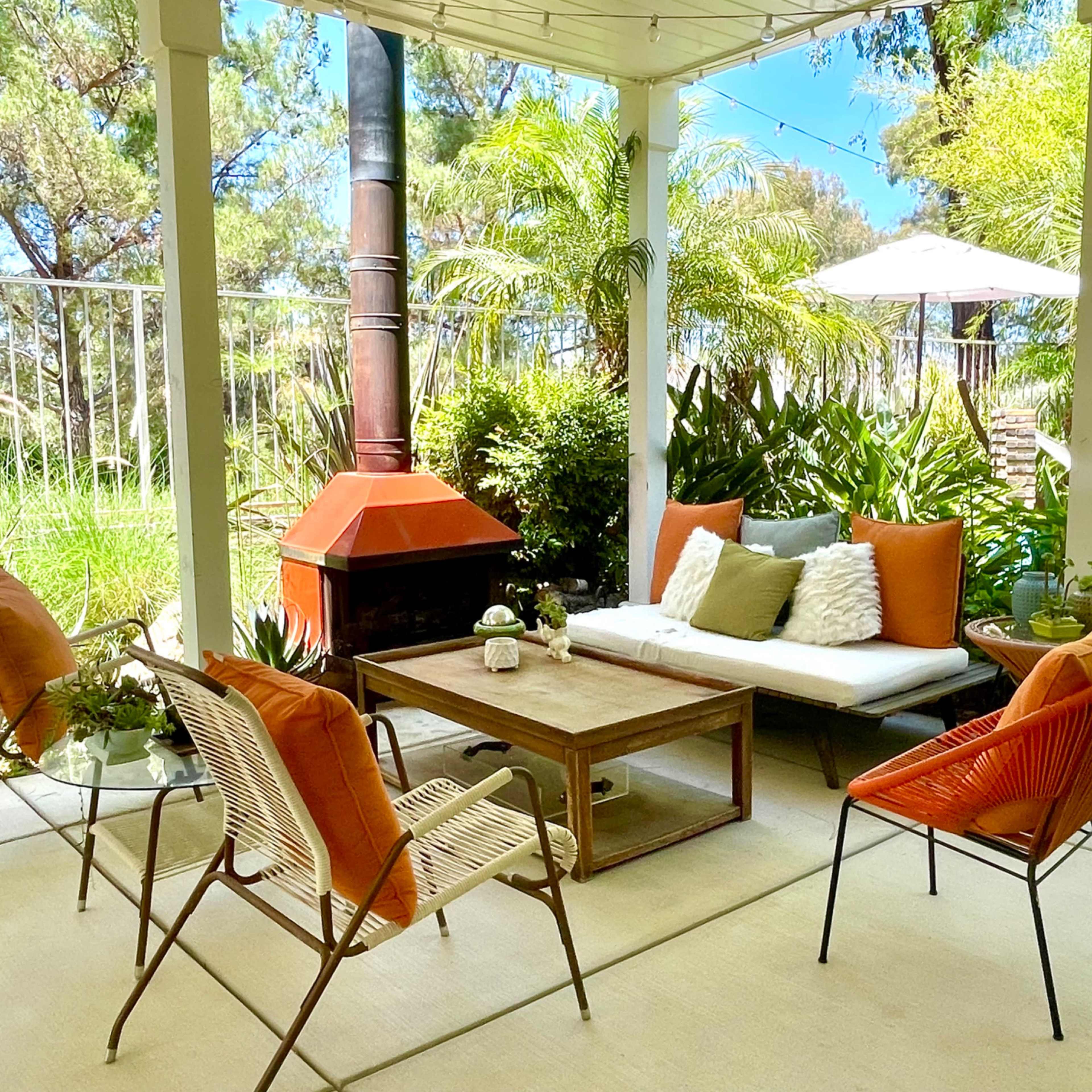 A patio area features a seating arrangement with a coffee table surrounded by chairs, a potted plant, and a fireplace, set in a landscaped garden with hammocks.
