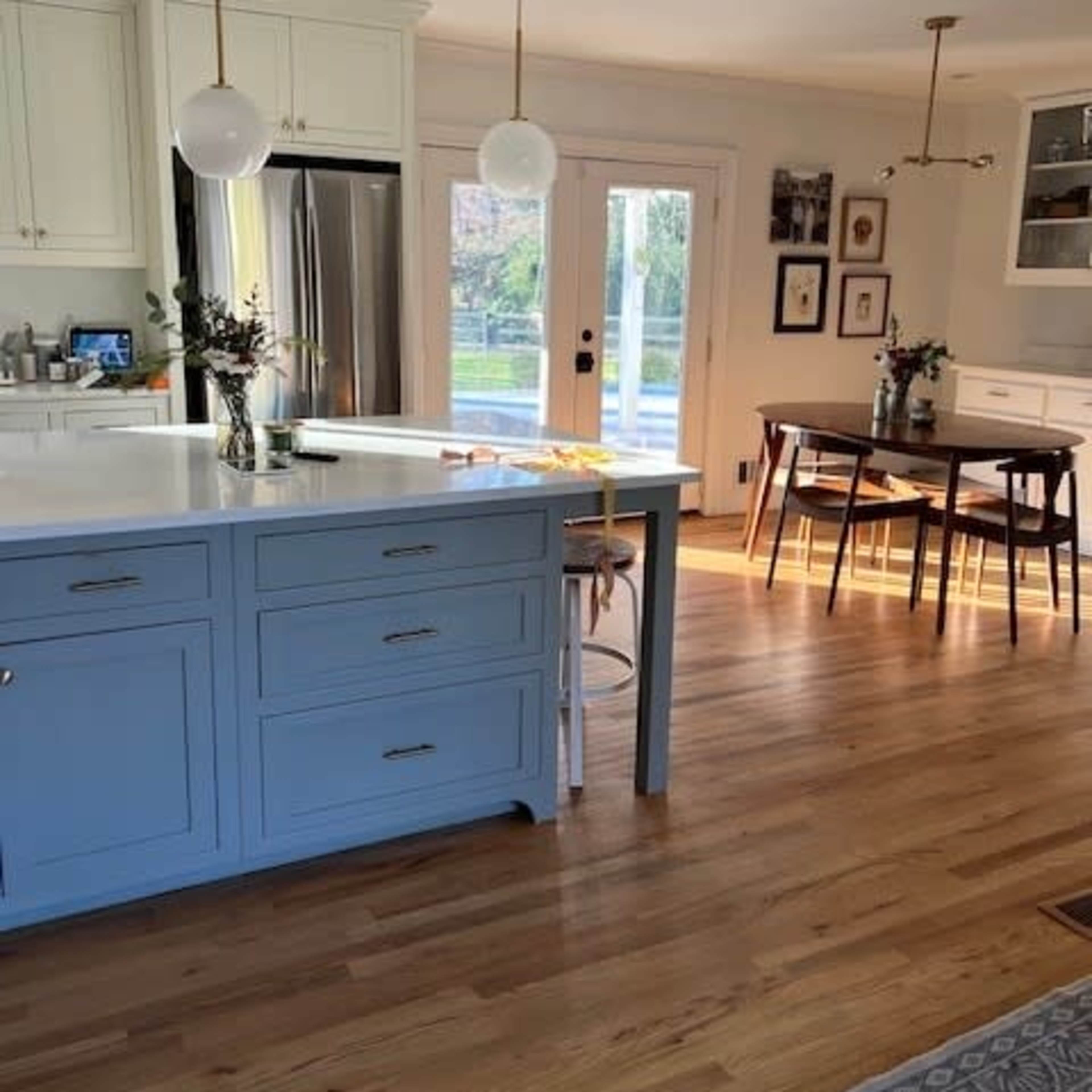 A bright, modern kitchen features a blue island, stainless steel appliances, and a dining area with a wooden table and chairs.
