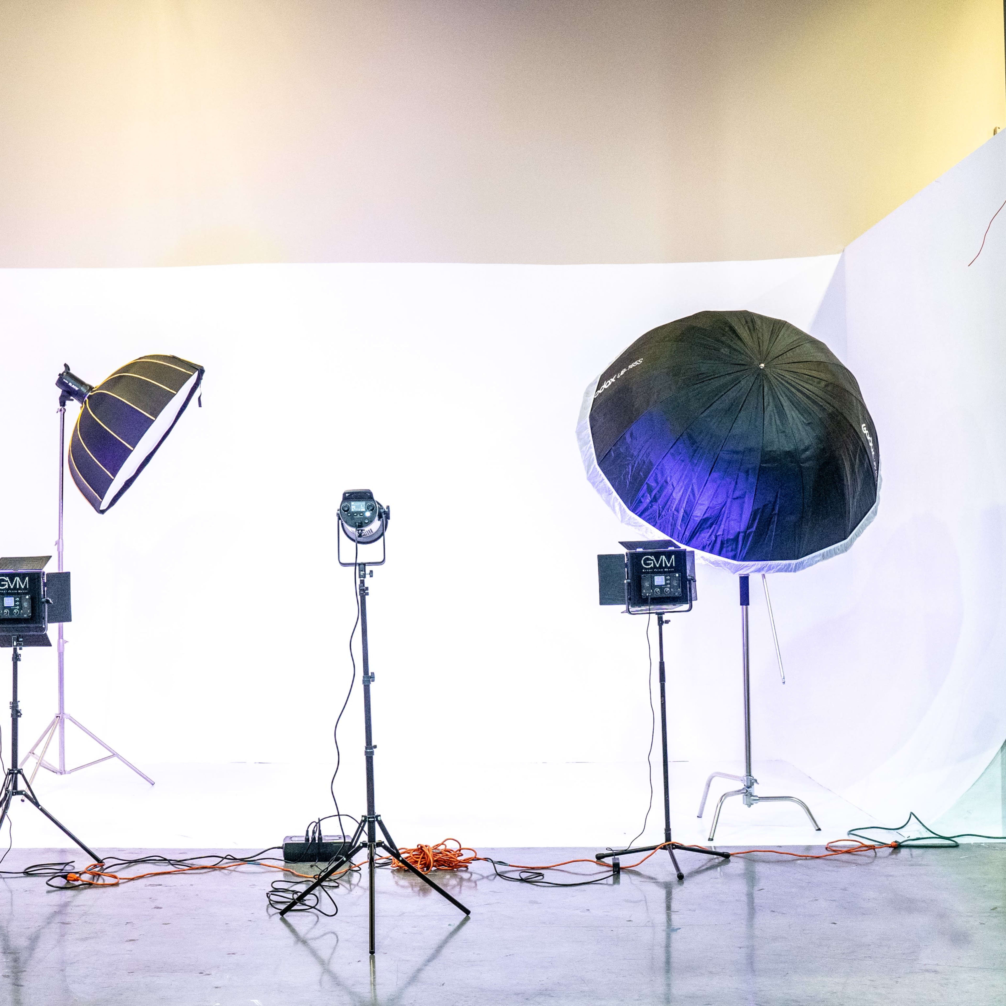 A photography studio setup features two large softbox lights and multiple light fixtures on a white backdrop.