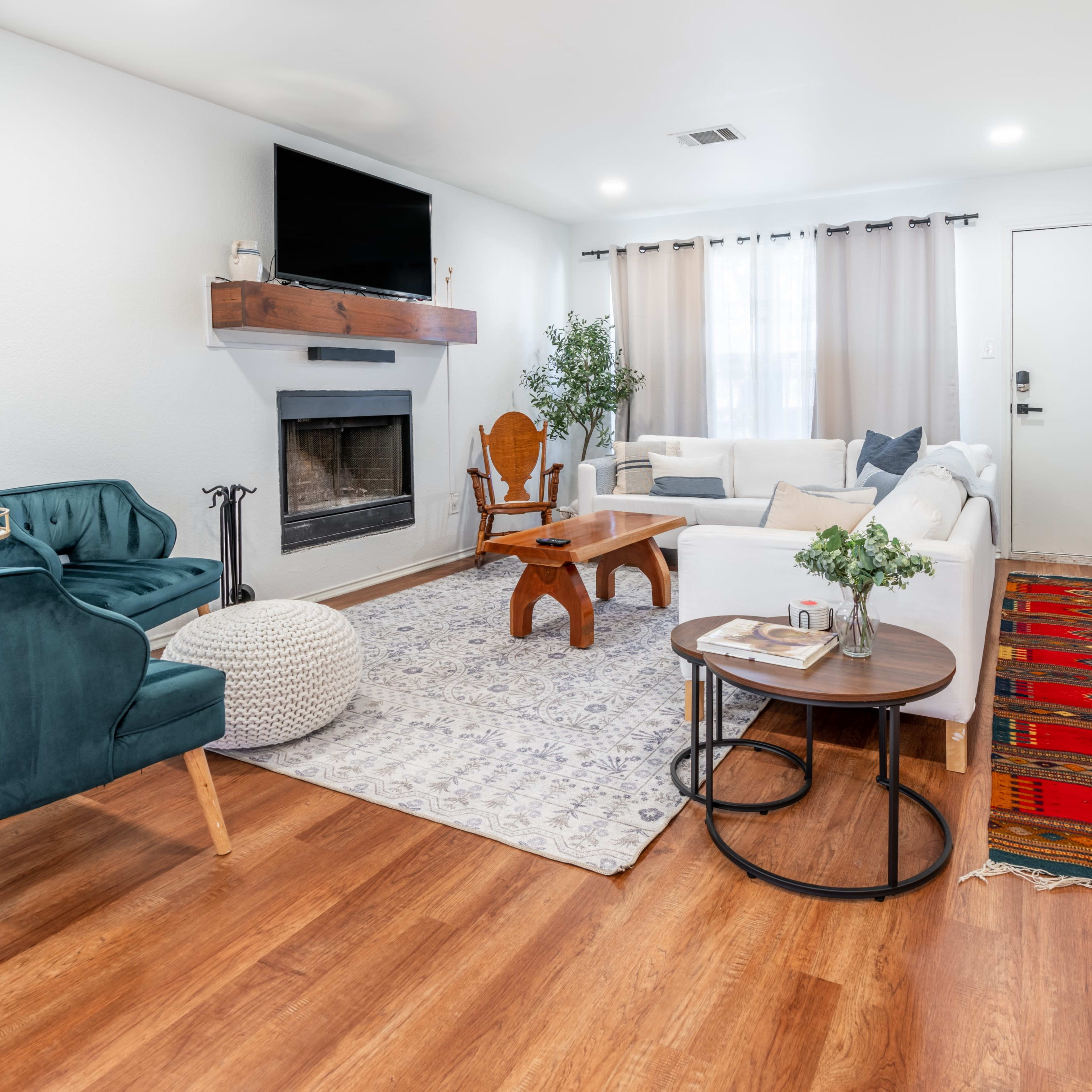 The living room features a cozy arrangement with a white sofa, wooden coffee table, and two teal chairs, set against a backdrop of a fireplace and a patterned area rug.