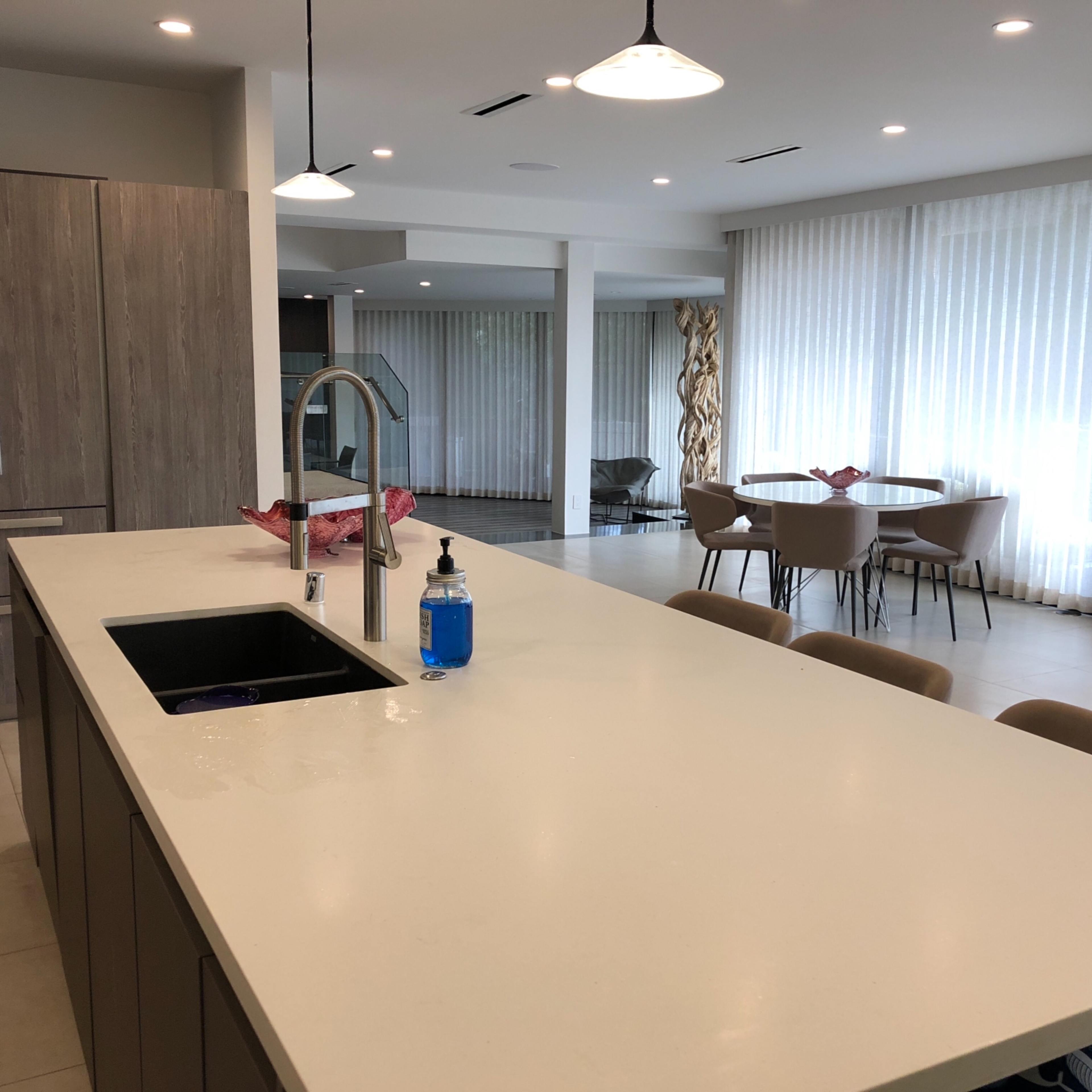 A modern kitchen features a white countertop with a sink, adjacent to a dining area with a round table and chairs.