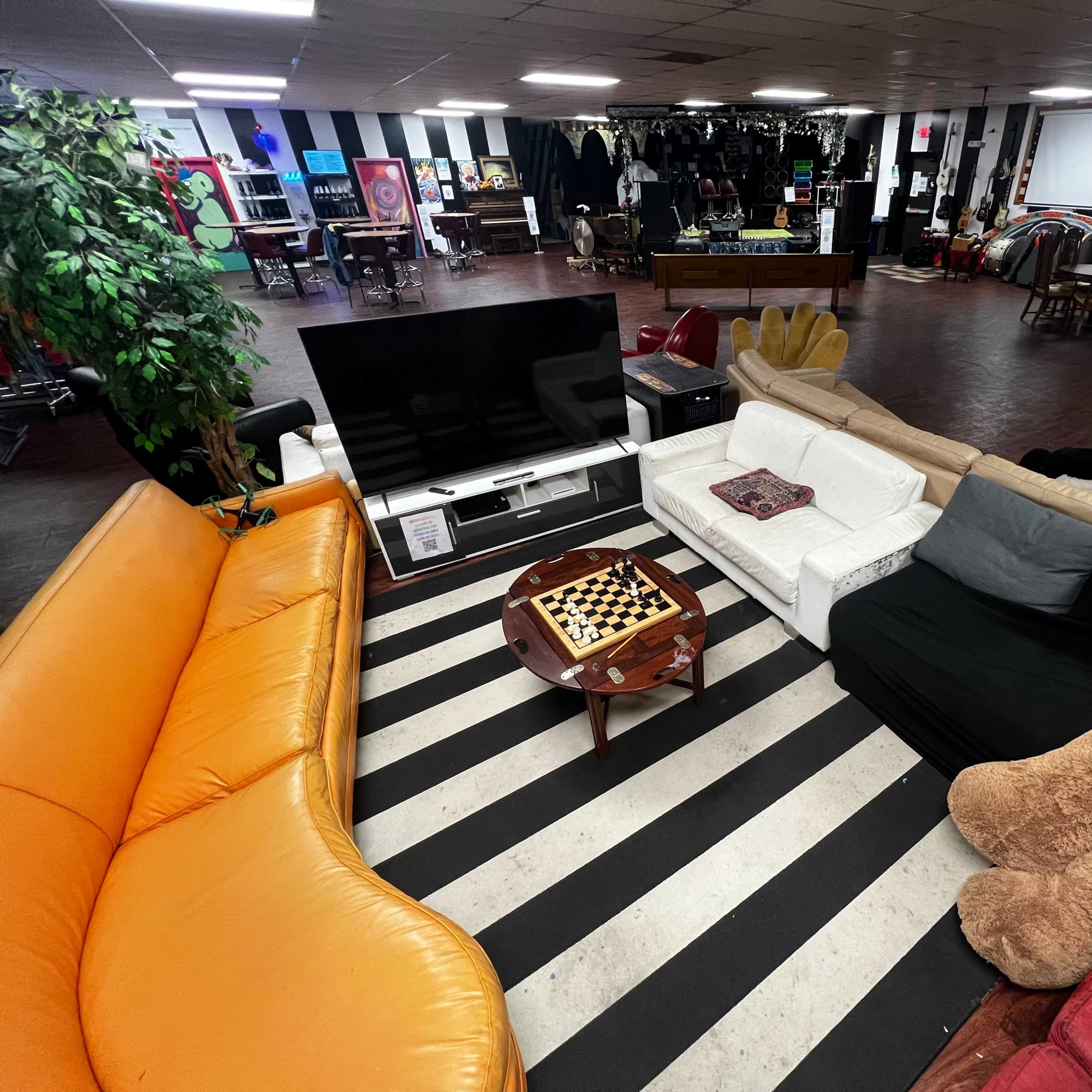 A large, open lounge area with various couches arranged around a coffee table on a striped rug, featuring a television and diverse artwork in the background.