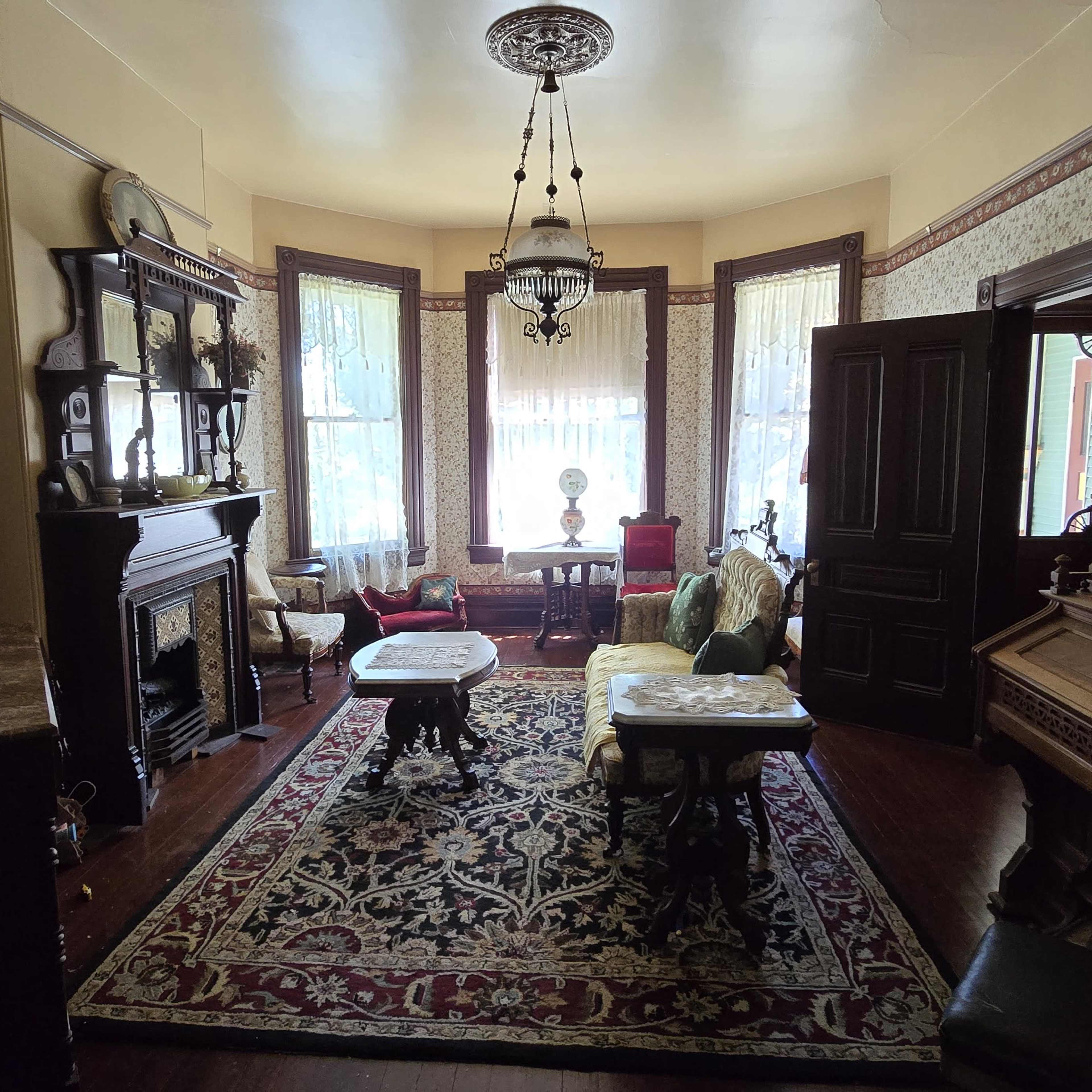 A Victorian-style living room with ornate furnishings, large windows, and decorative wallpaper.
