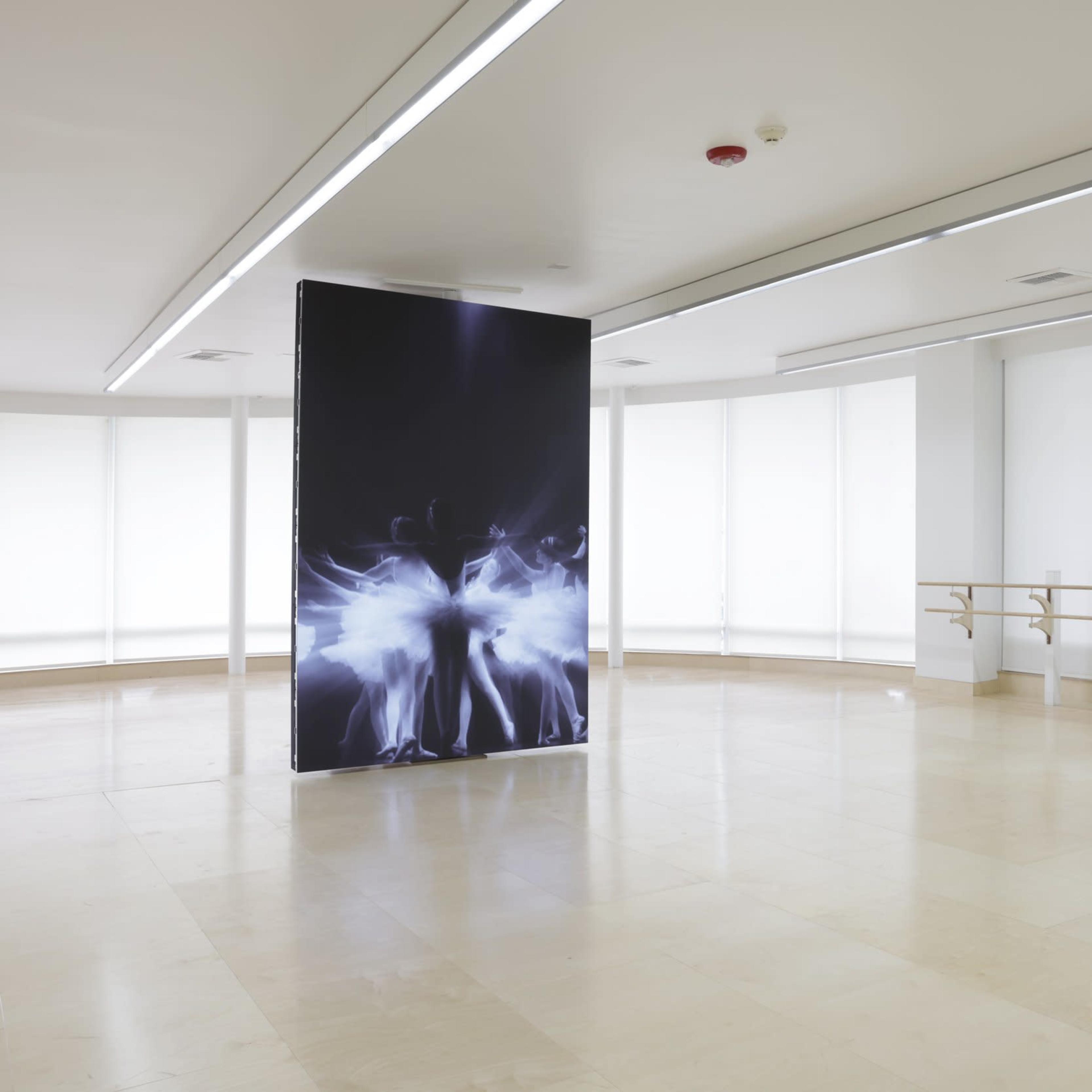 A spacious, minimalist dance studio with large windows and a central display panel featuring a graphic design.