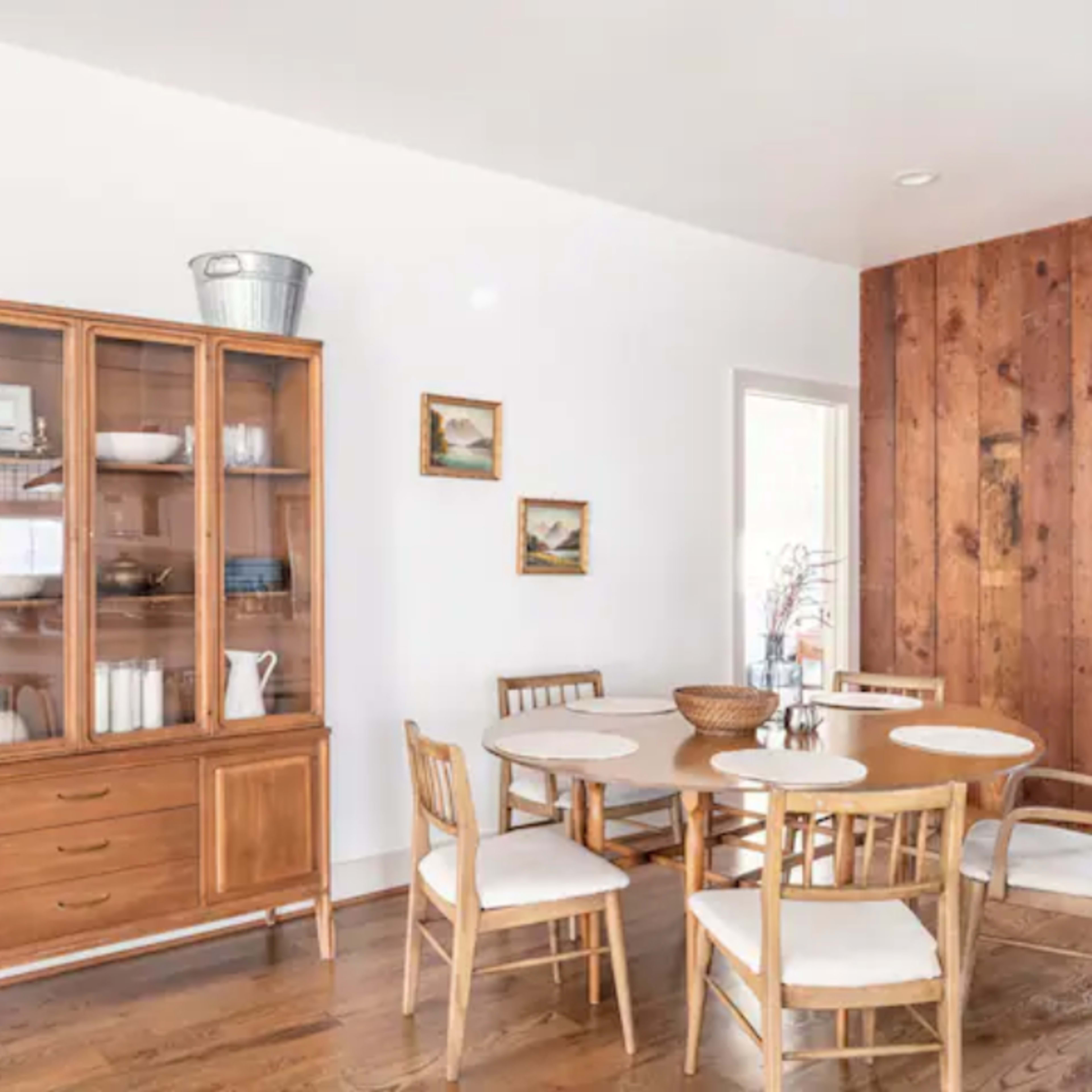 A dining area featuring a wooden table surrounded by chairs, a glass-front cabinet, and a wall made of wooden panels.