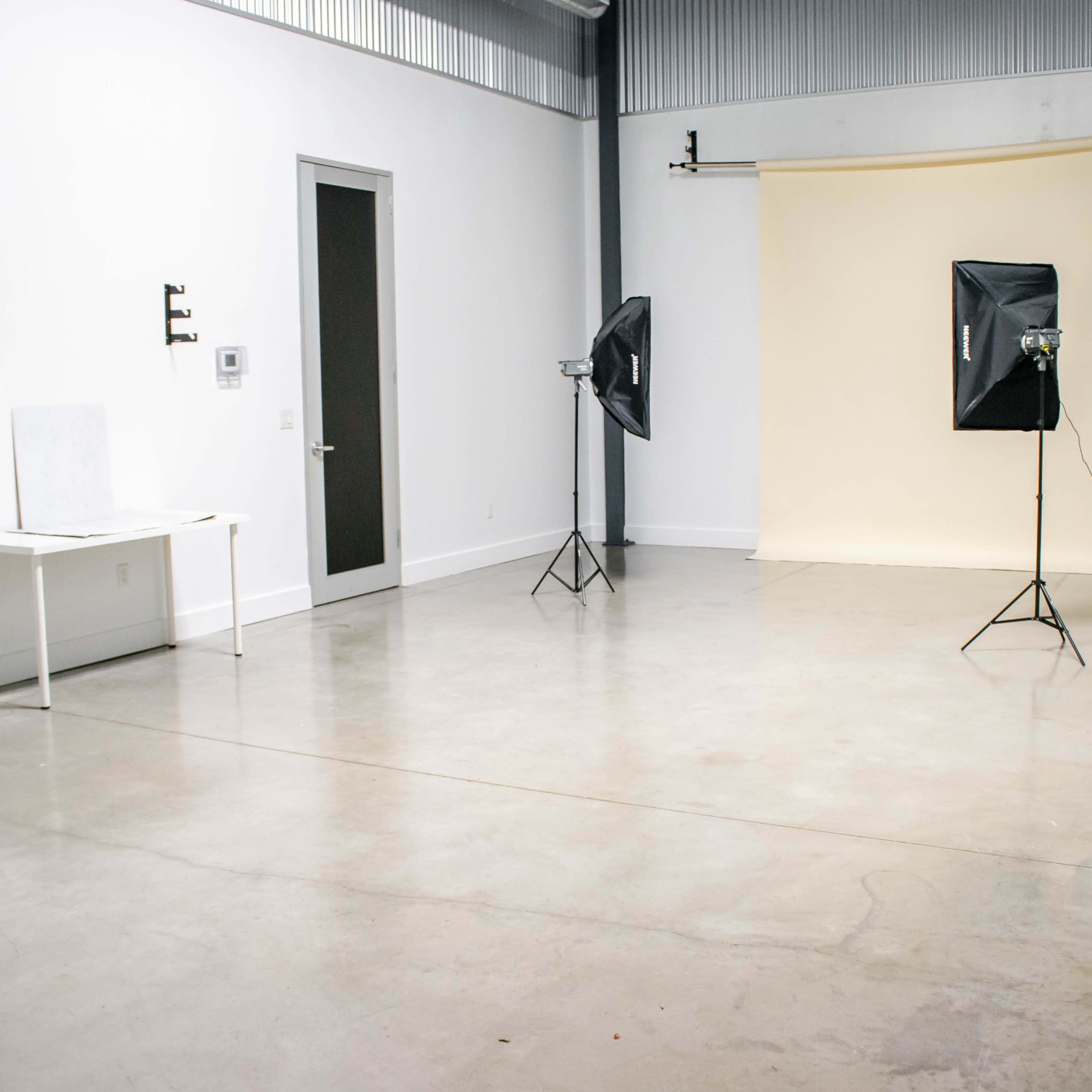 The scene shows a spacious, empty studio with a light-colored backdrop, two softbox lights, and a white table against a wall.