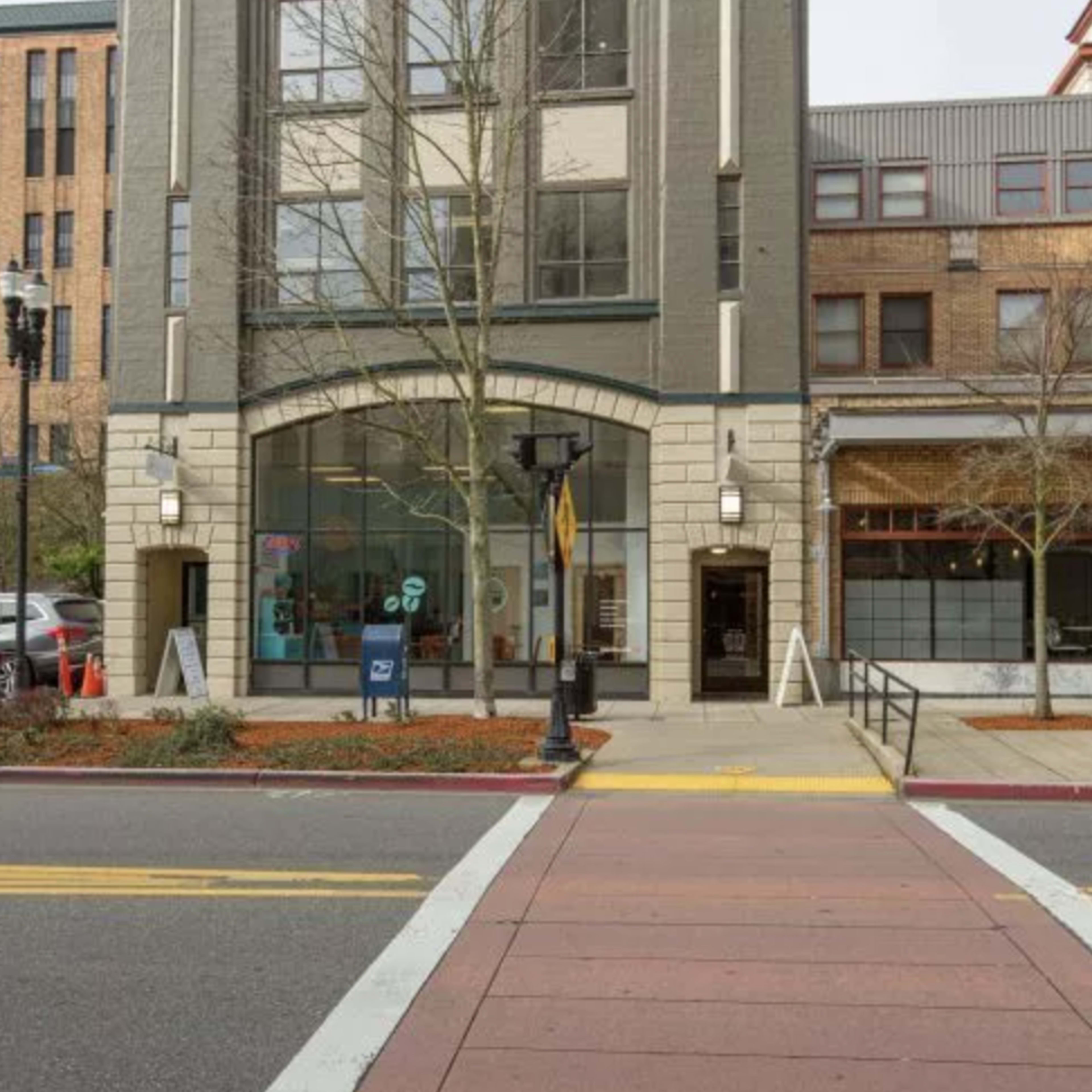 A multi-story urban building with large windows and a central archway entrance, situated across a street with a crosswalk.