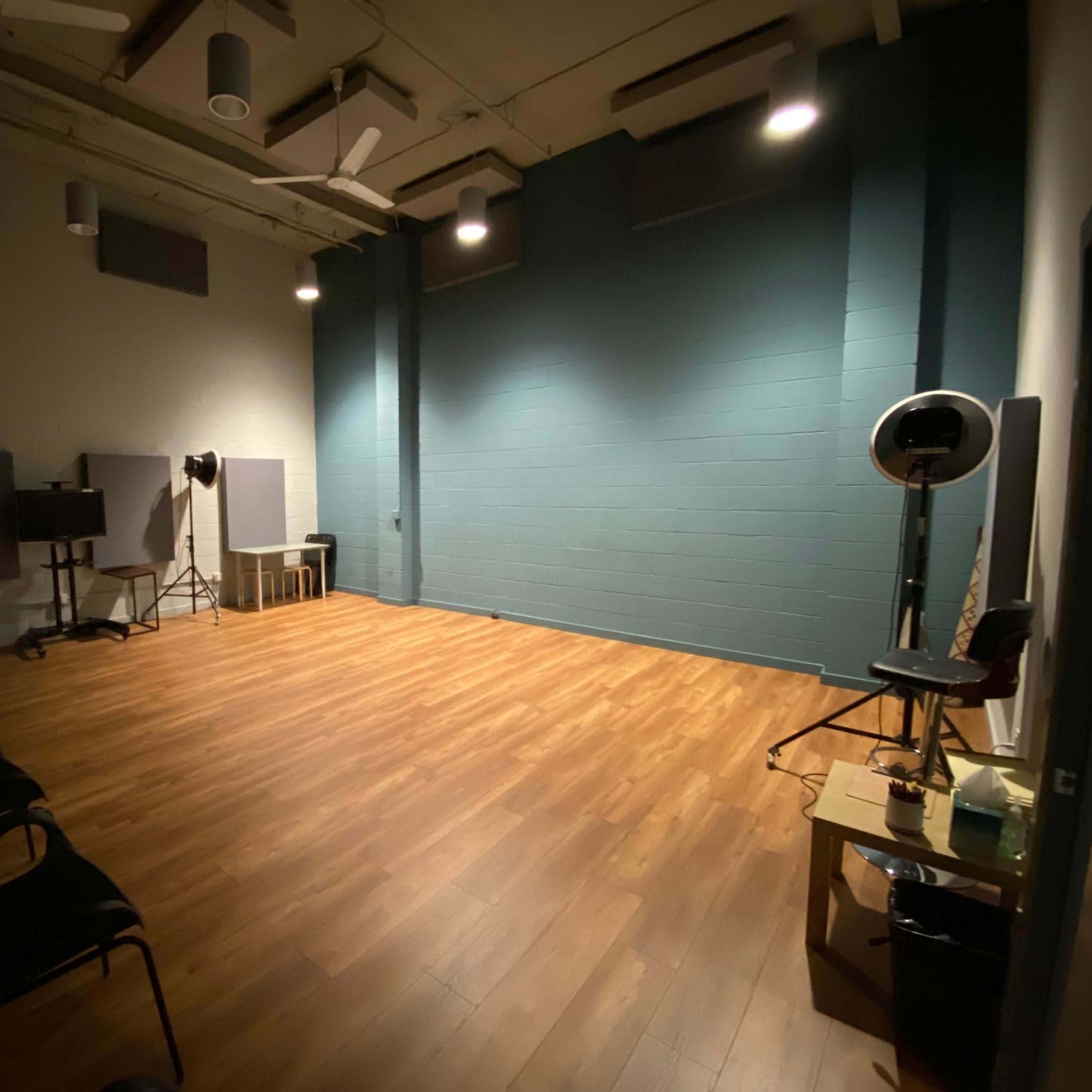 An empty studio space features a wooden floor, a painted blue wall, and several adjustable lights mounted on the ceiling.