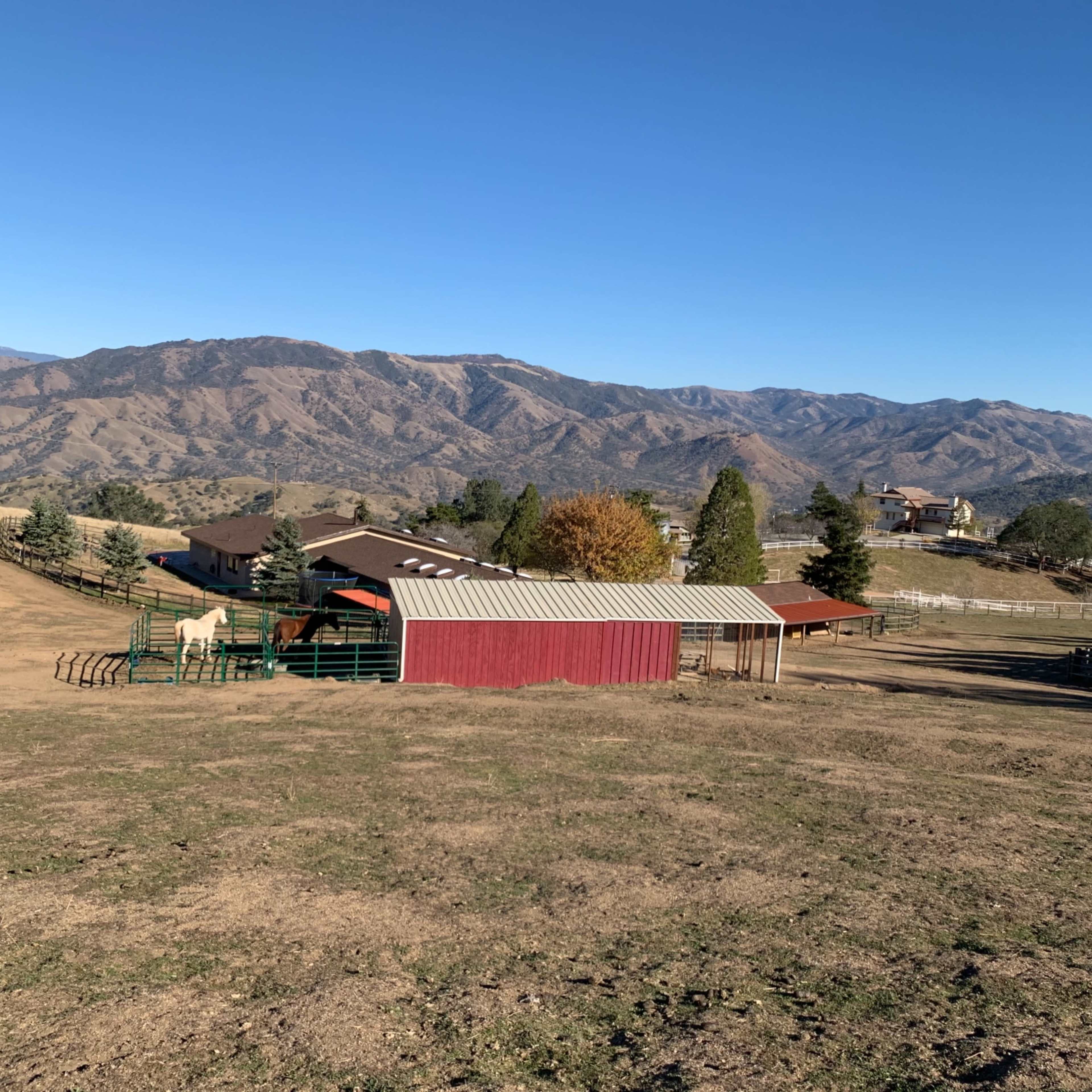 A rural landscape with a red barn, a fenced area, and distant mountains under a clear blue sky.