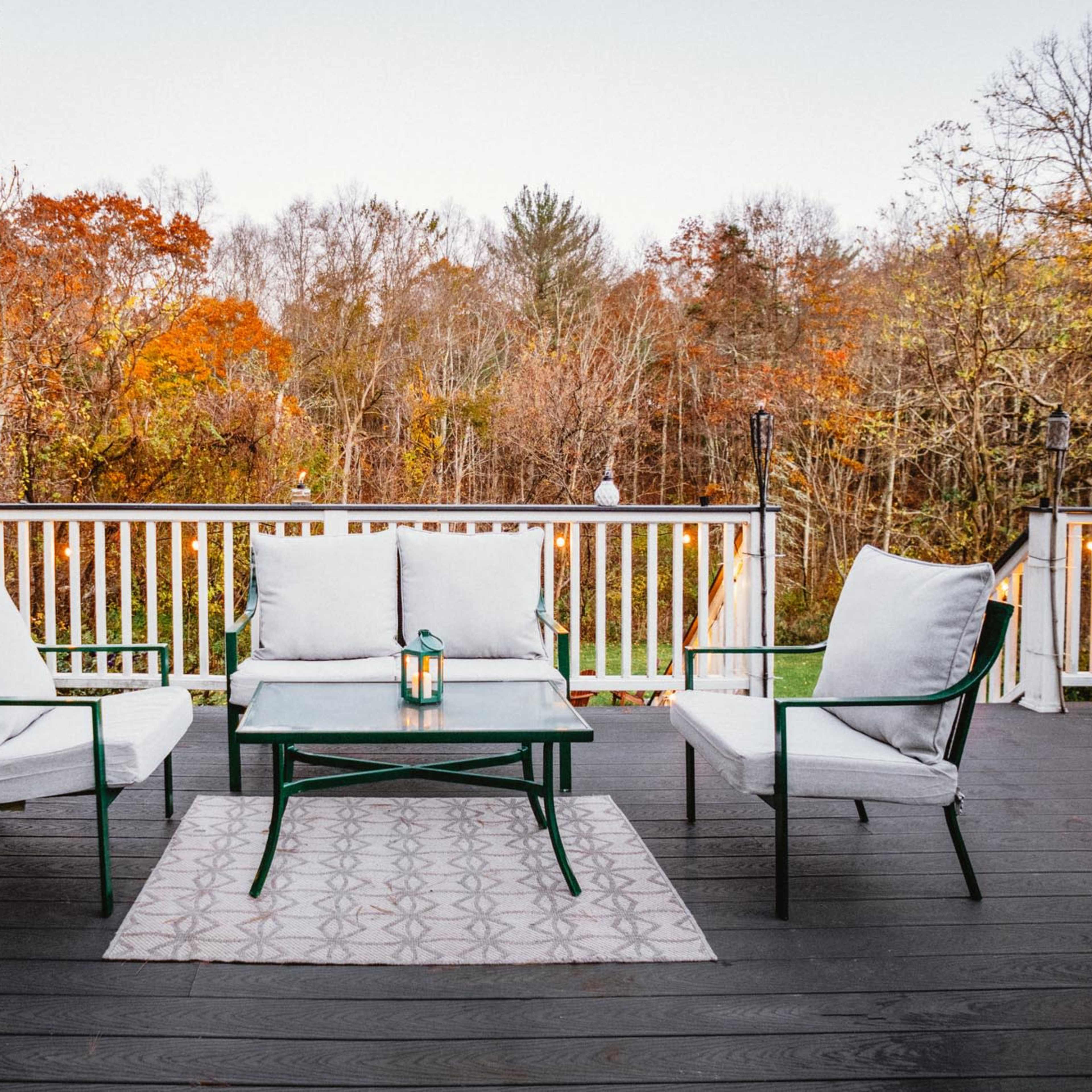 A patio area features a small table and three chairs, surrounded by trees with autumn foliage.