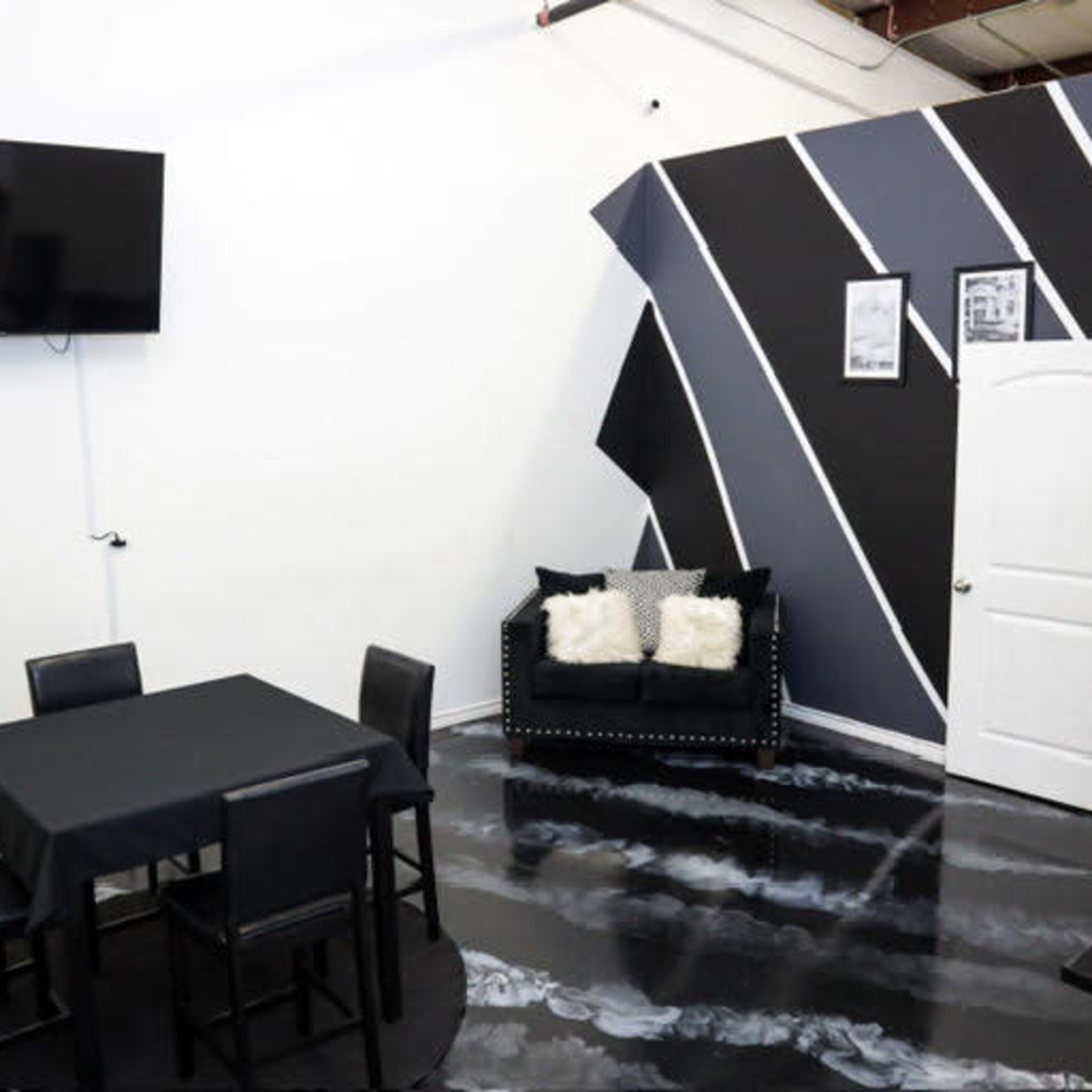 A modern room with a square black table and four chairs, a couch with cushions, a mounted television, and a painted accent wall featuring diagonal black and gray stripes.