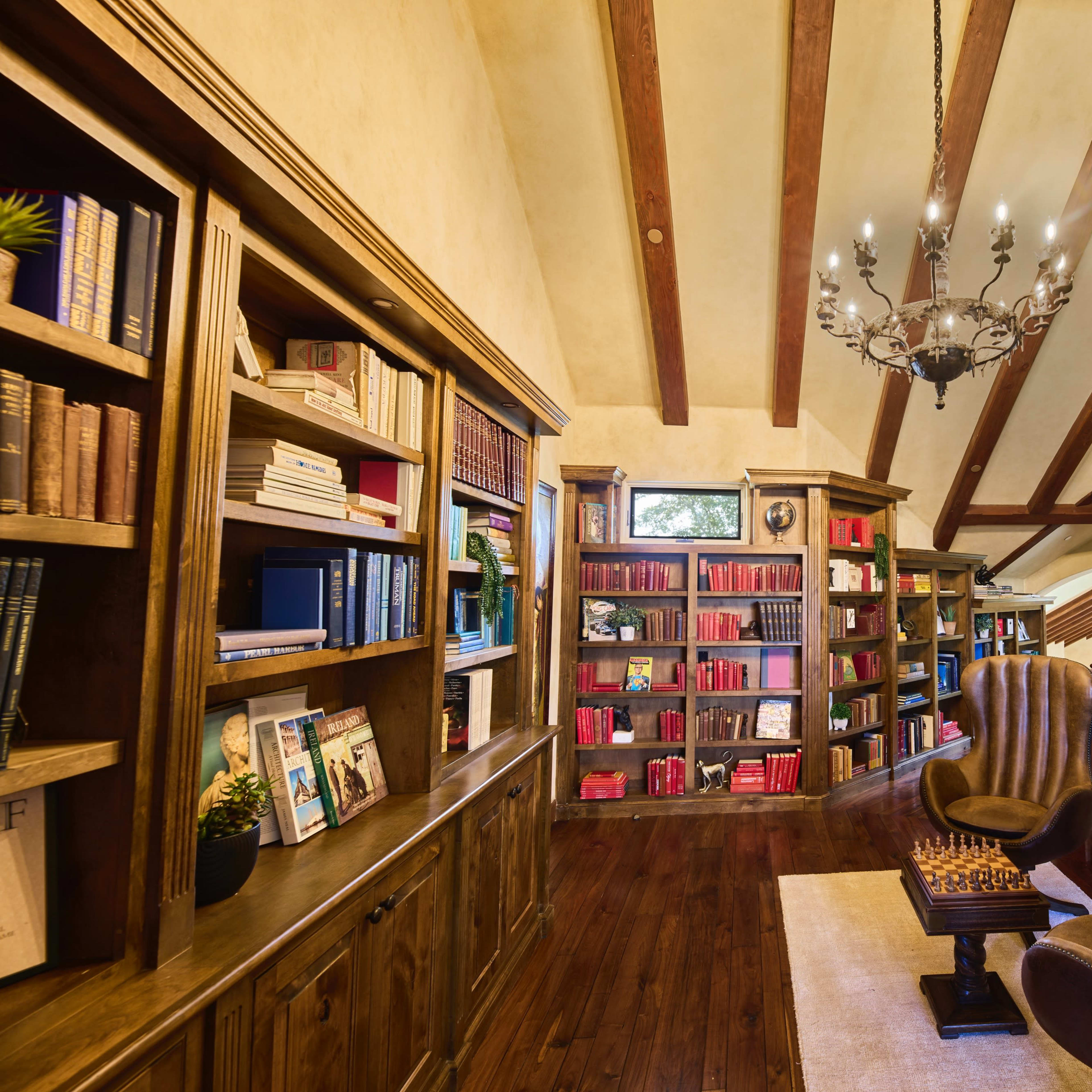 A well-appointed library with wooden shelves filled with books and cozy seating, illuminated by a chandelier.