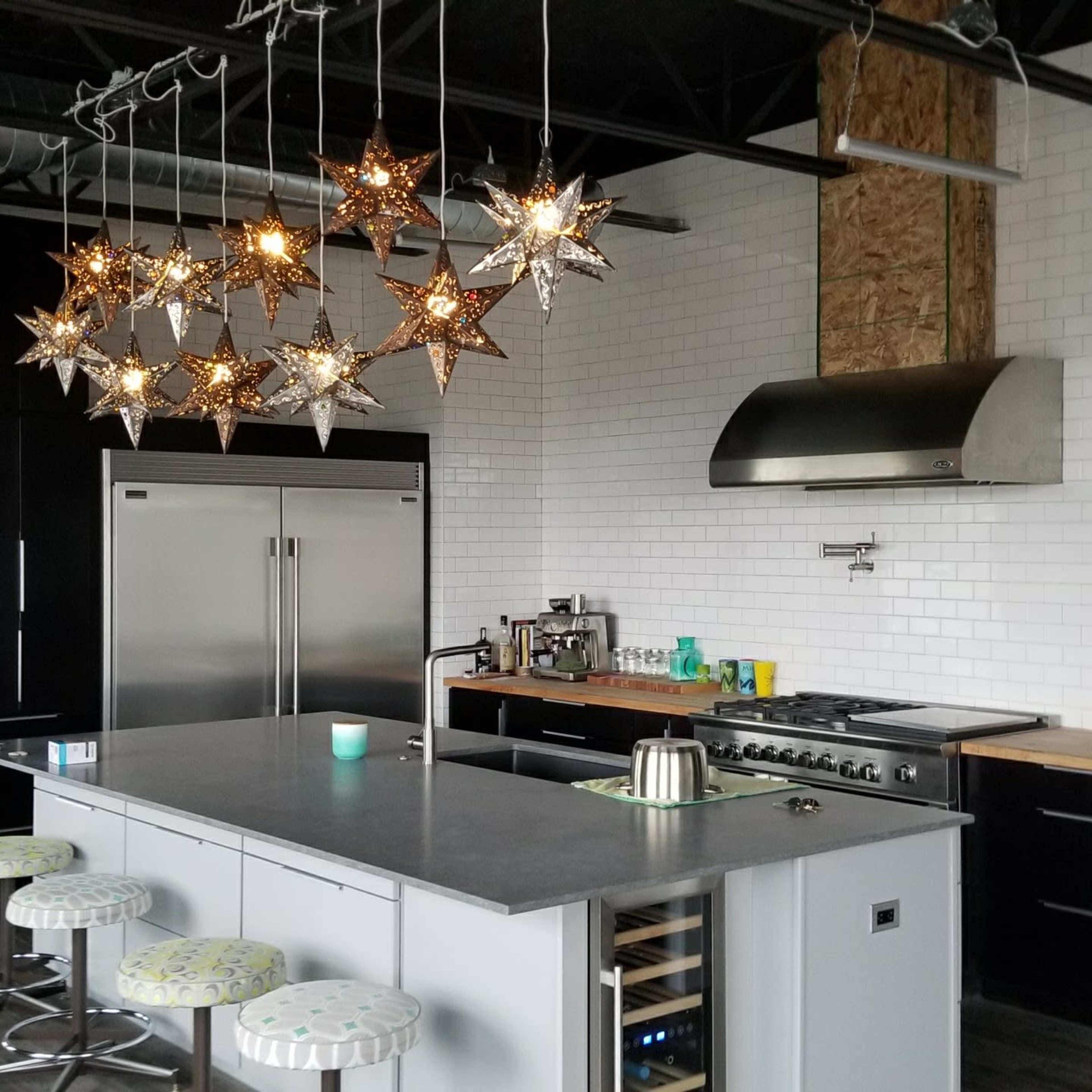 The kitchen features a centrally located island with stools, surrounded by black cabinetry and hanging star-shaped lights.