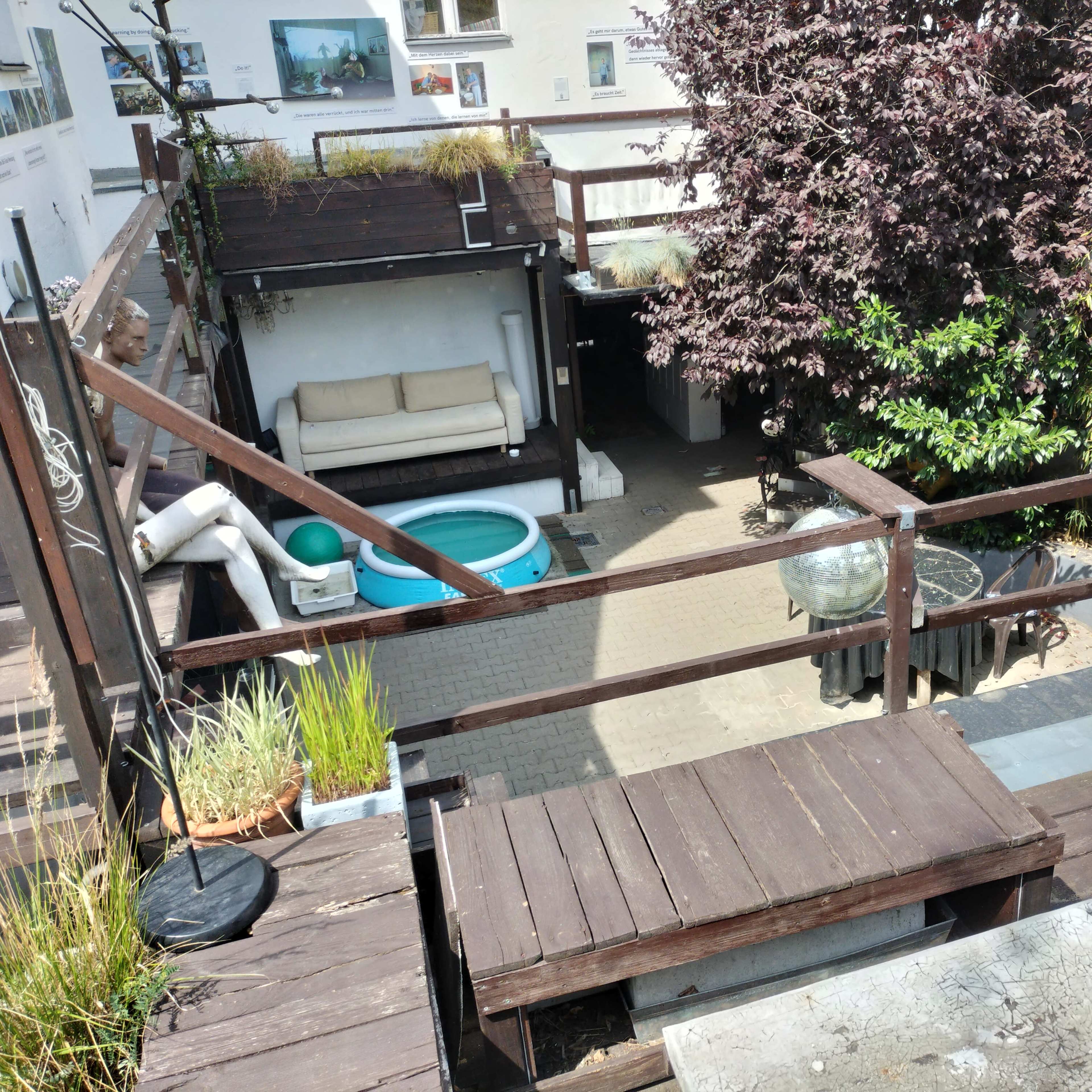 A rooftop terrace with wooden decking, a small pool, a seating area, and various potted plants.