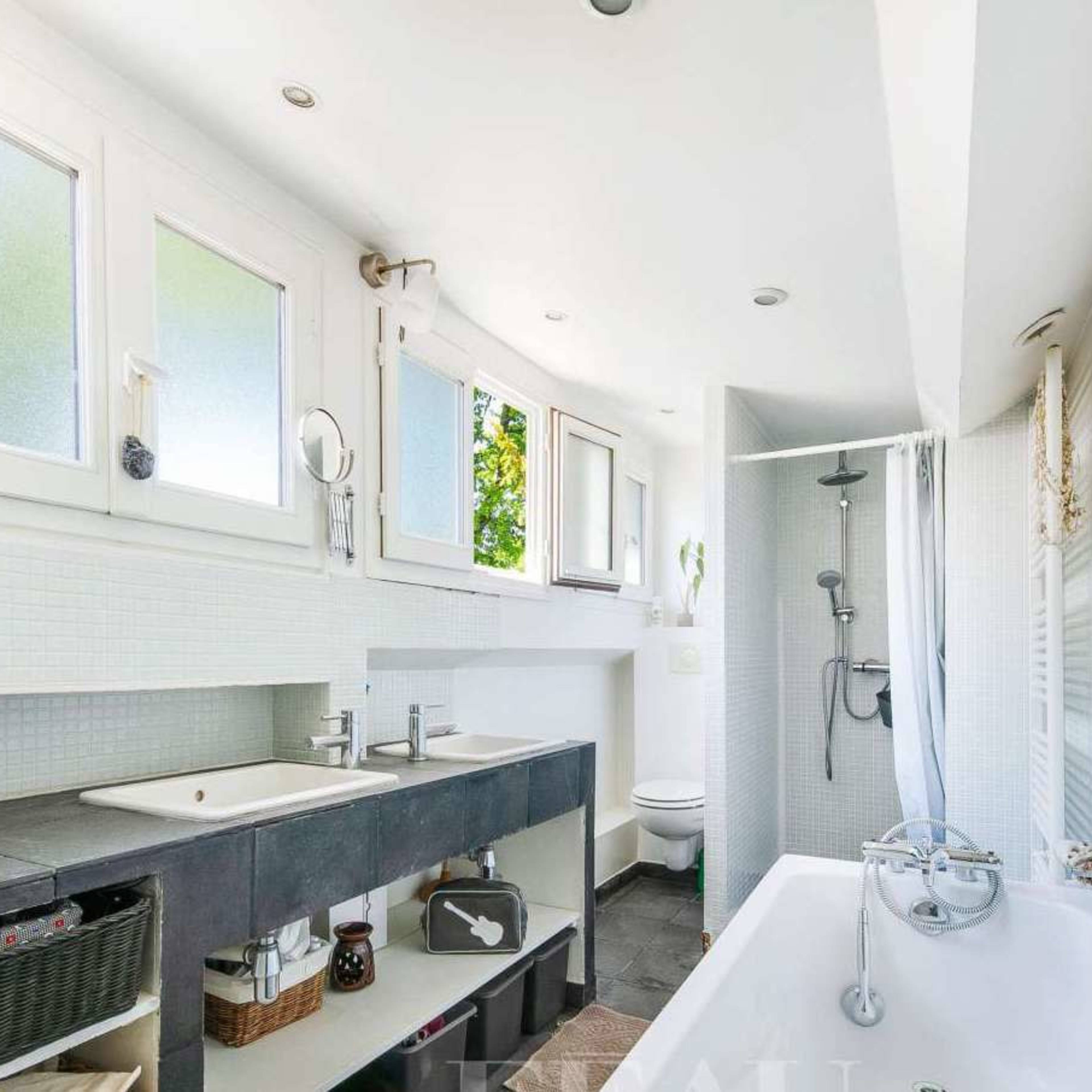 A modern bathroom features a freestanding bathtub, a double sink vanity, a glass shower, and large windows allowing natural light.