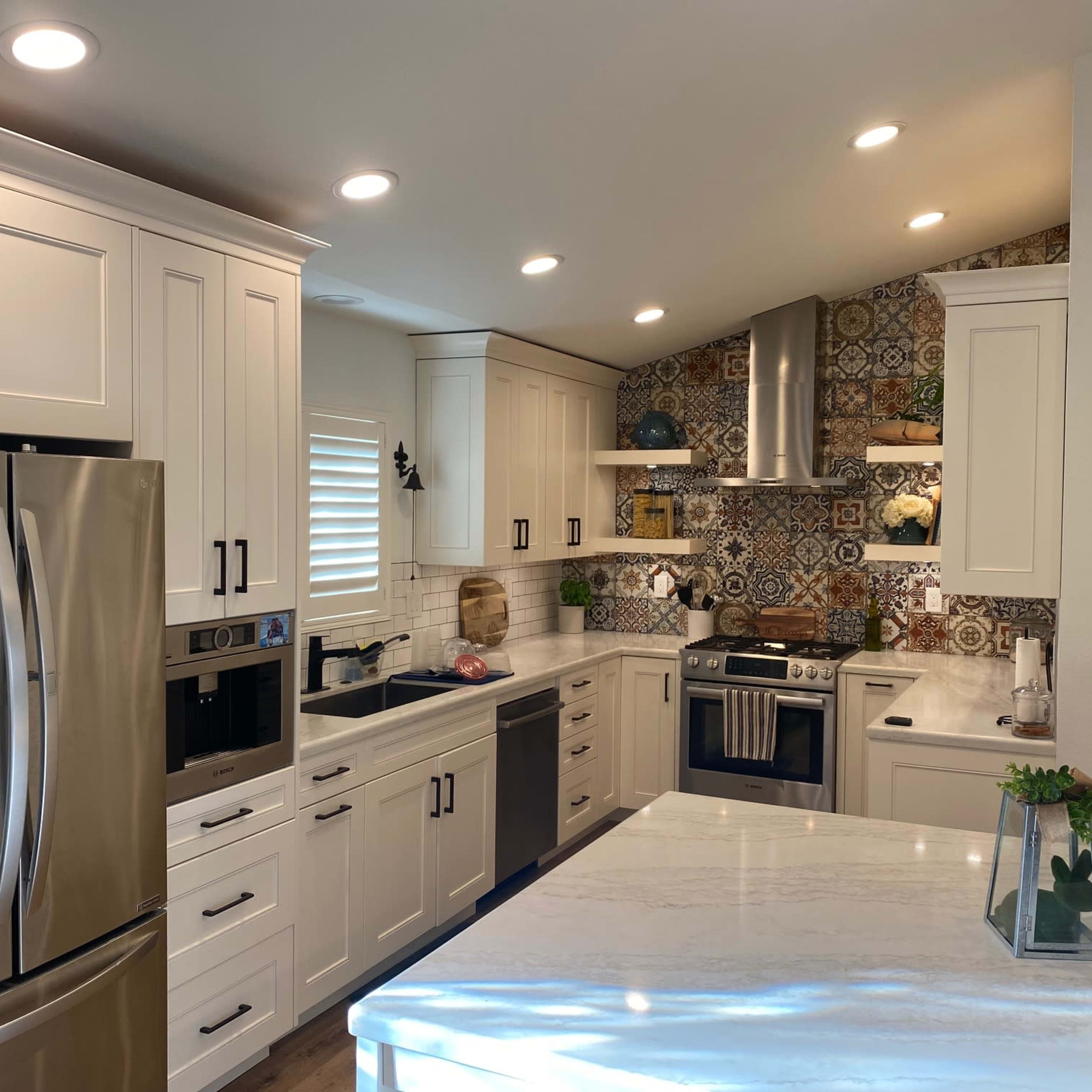 A modern kitchen features white cabinetry, stainless steel appliances, and colorful tile accents on the wall.
