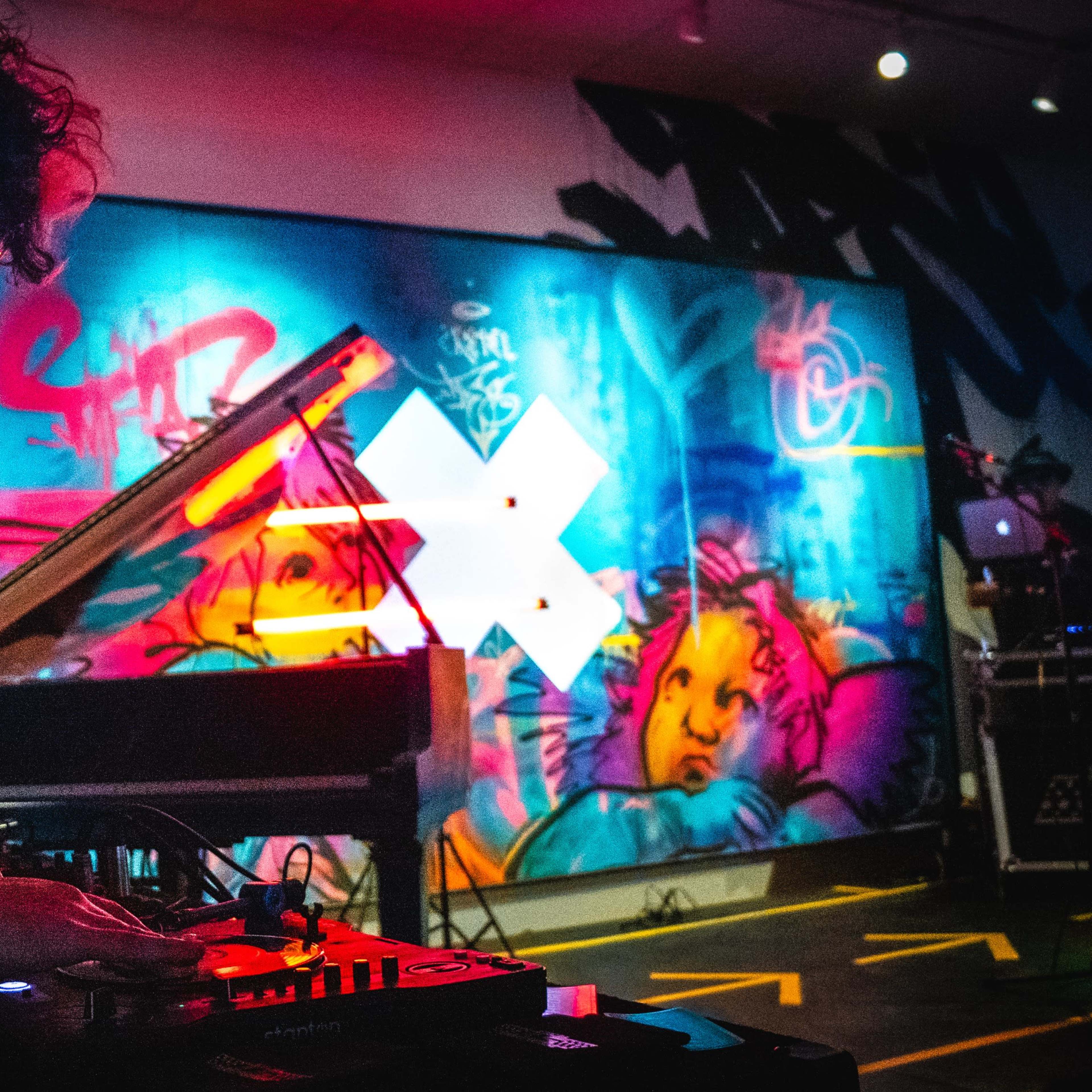 A musician operates a turntable in front of a brightly colored mural during a live performance.