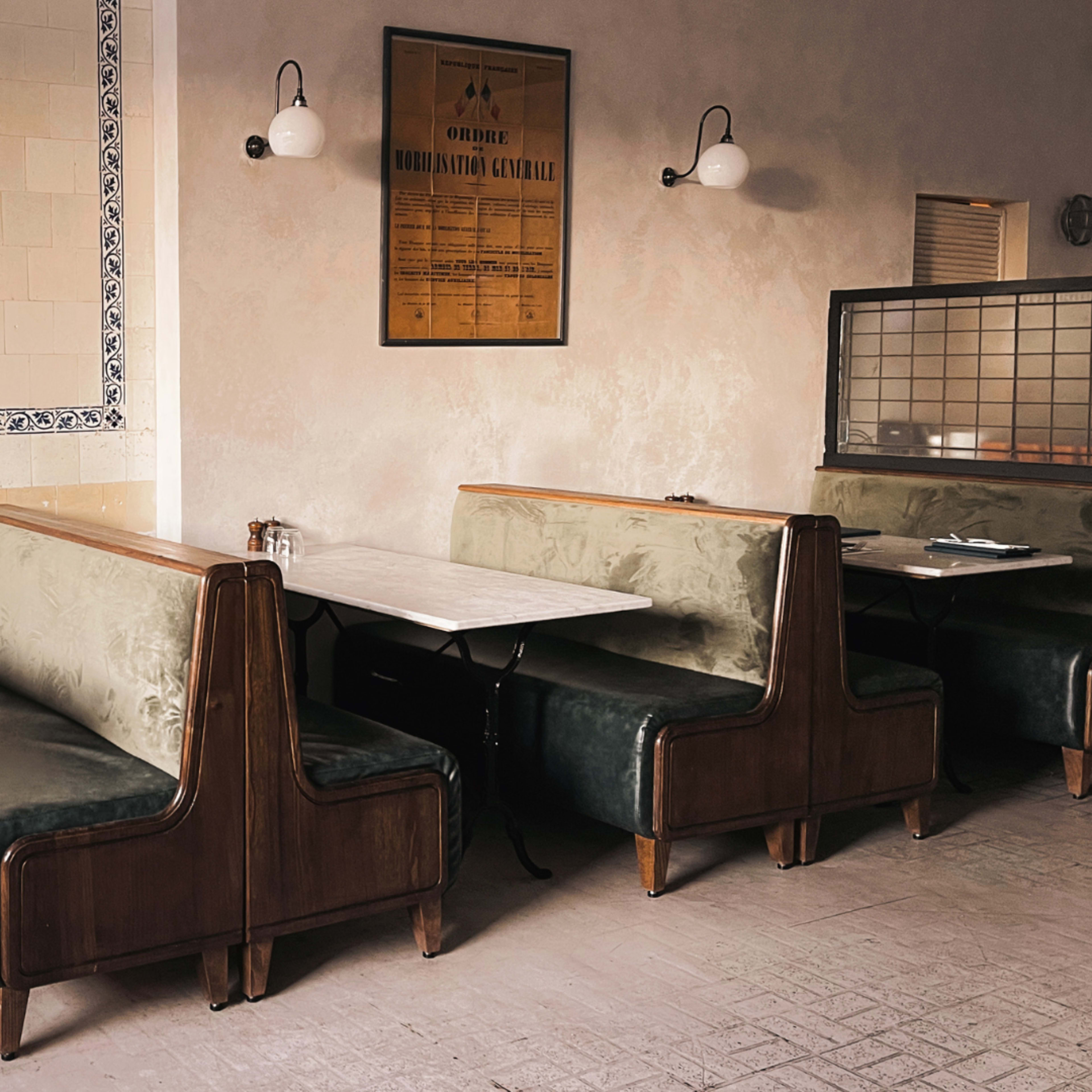 A restaurant interior with wooden booth seating, marble-topped tables, and a tiled wall adorned with a framed vintage poster.