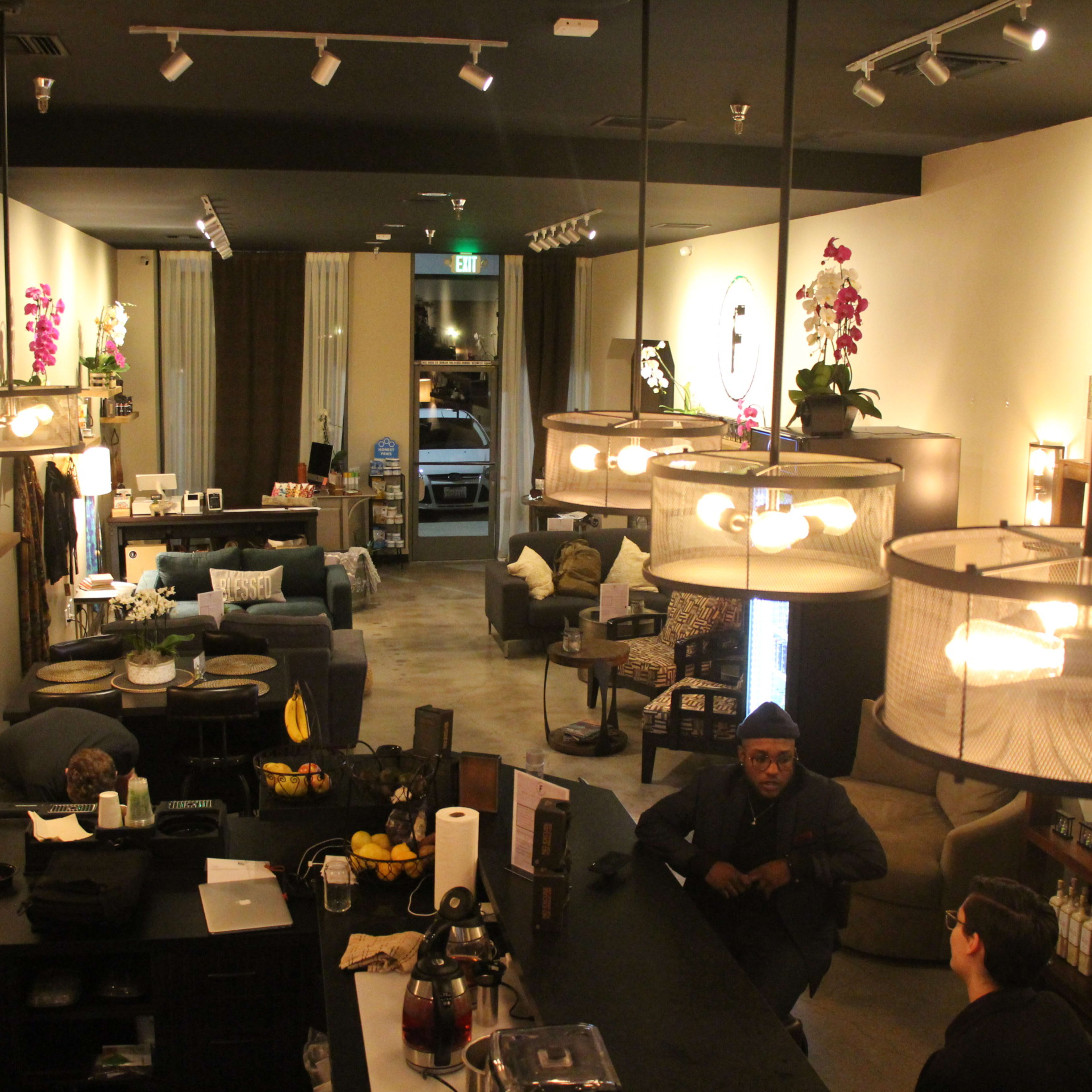 A stylish café interior with seating arrangements, a bar area, and decorative plants, illuminated by pendant lights.