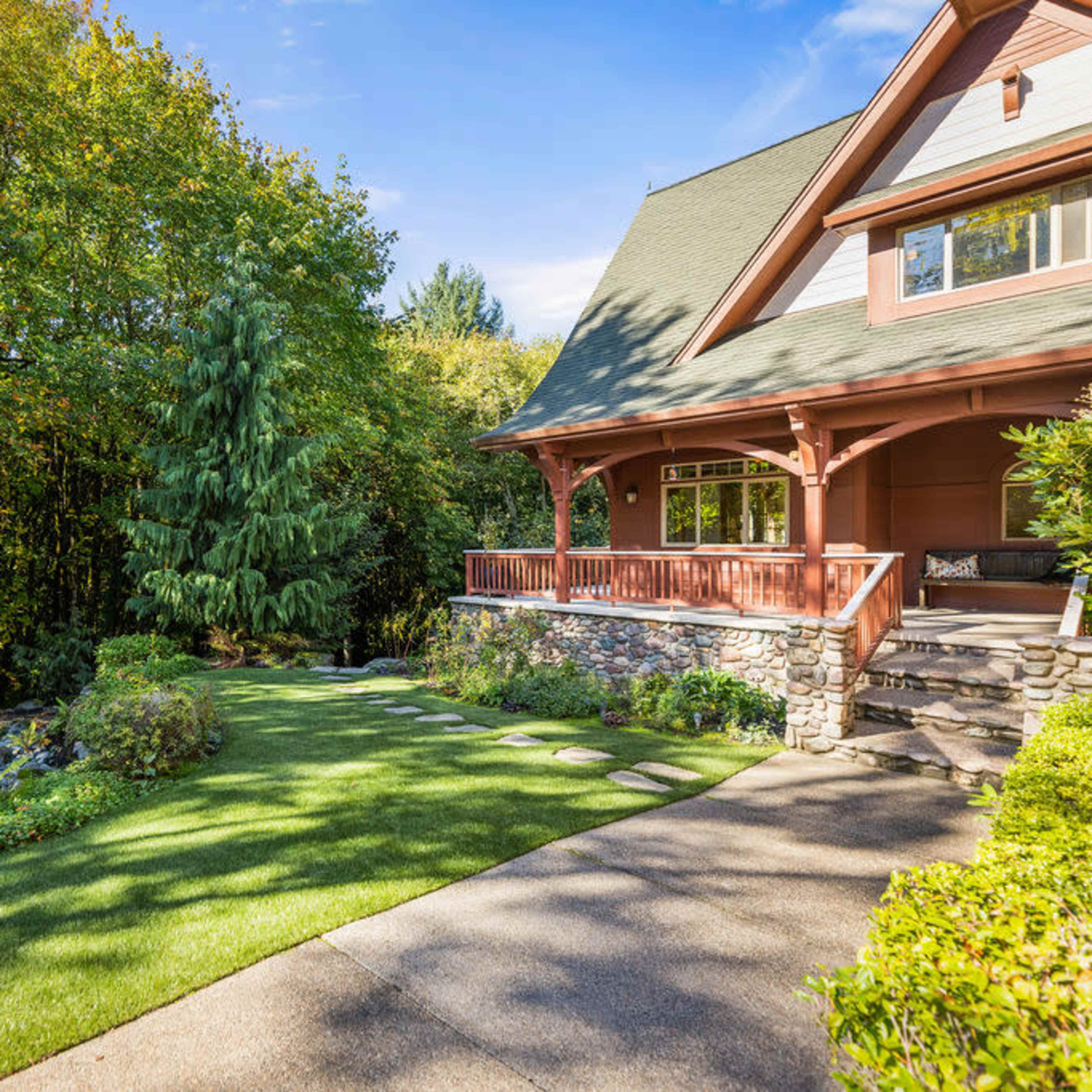 A two-story house with a porch is surrounded by lush greenery and a well-maintained lawn.