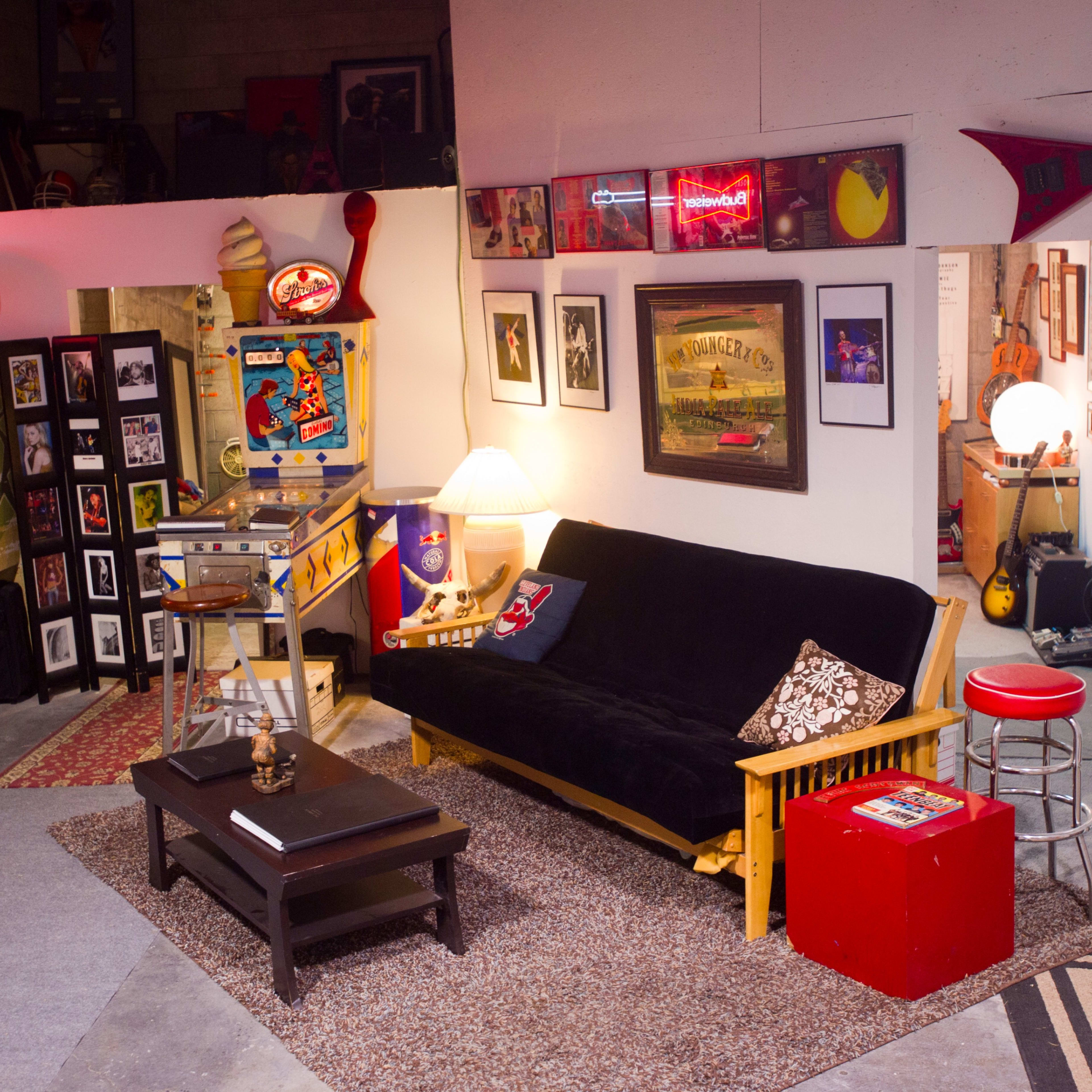 A cozy room with a black futon, a coffee table, posters on the walls, and a vintage jukebox illuminated by neon lights.