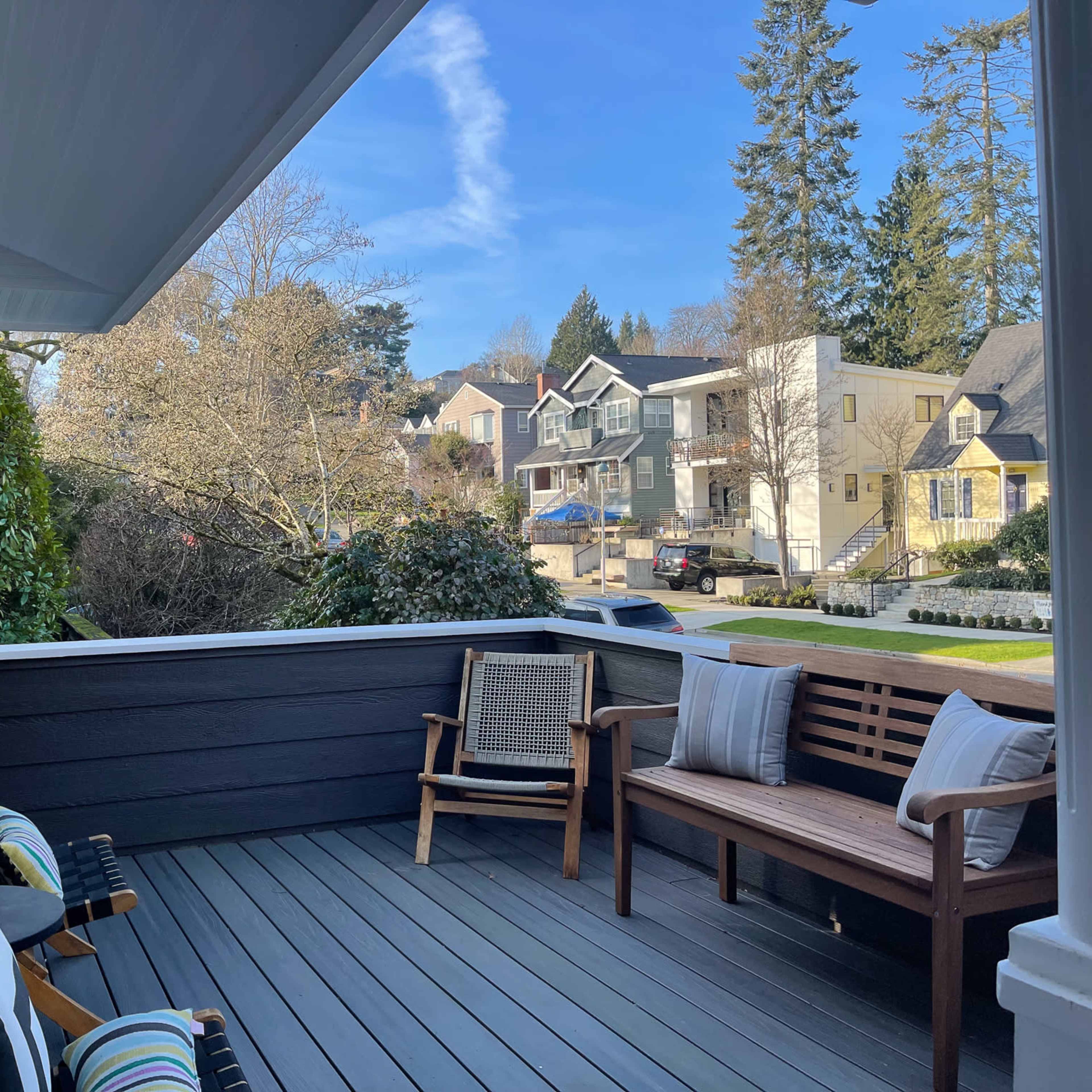 A porch with wooden flooring and seating that overlooks a neighborhood with houses and trees.