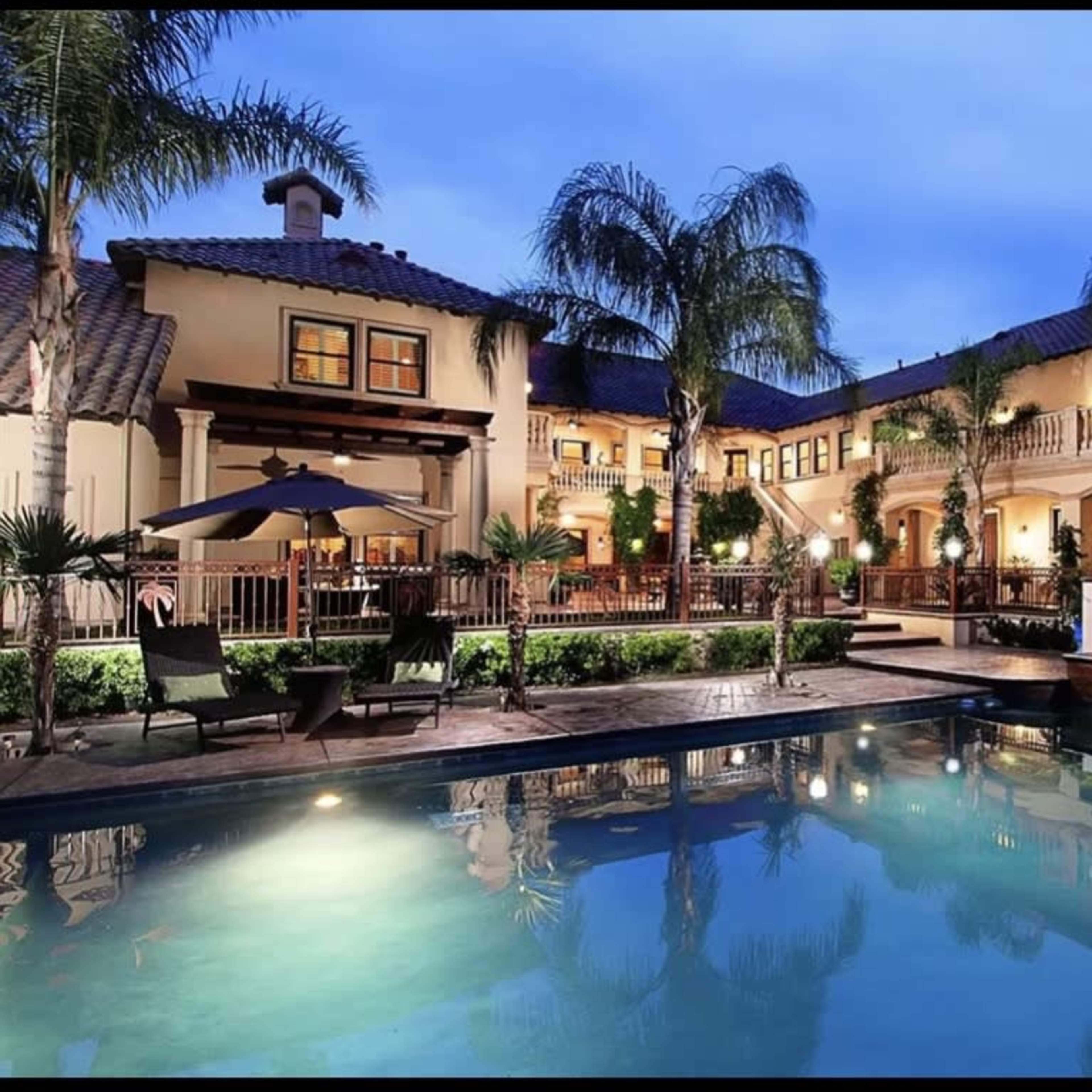 A large, two-story mansion with a pool and palm trees in the foreground.