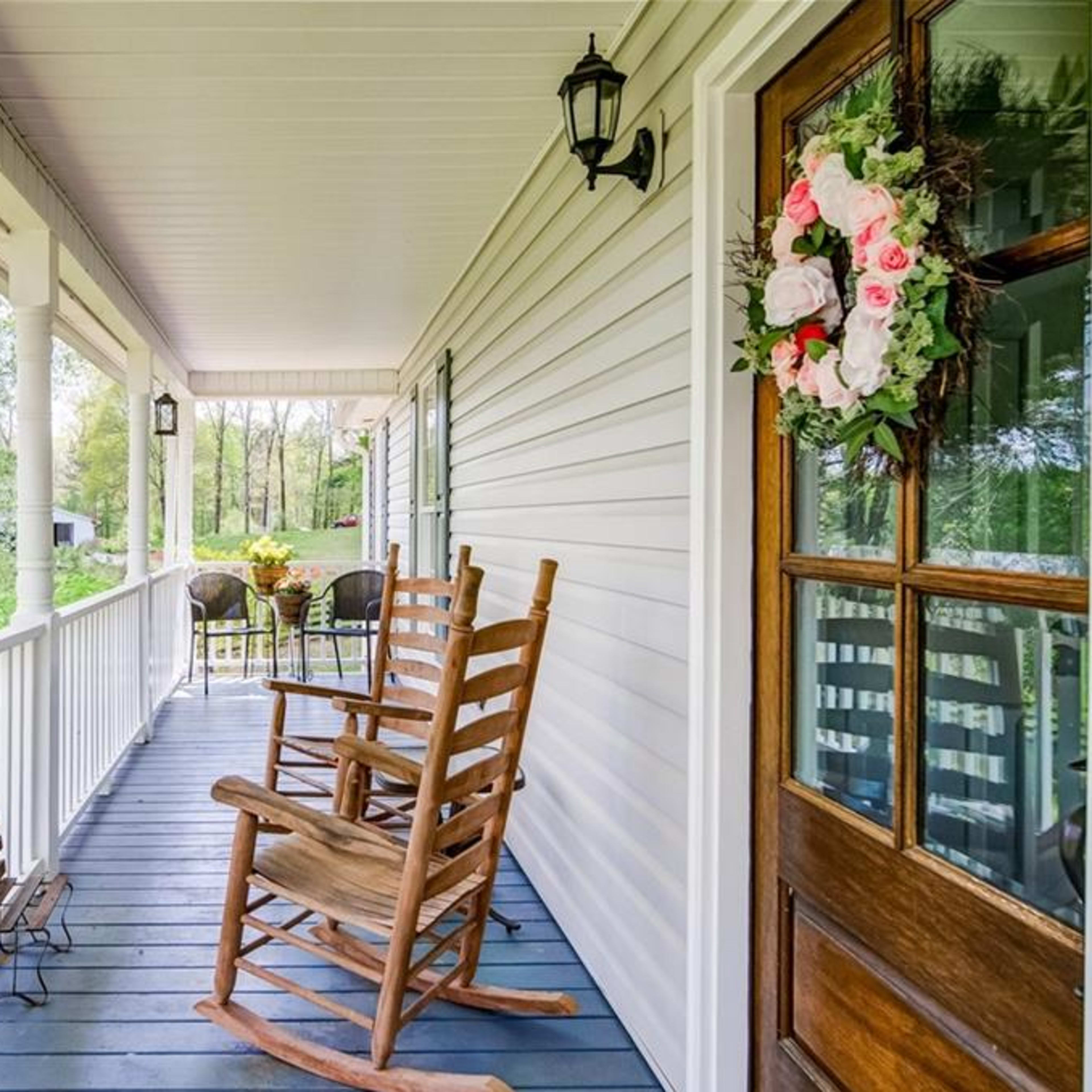 A porch with two rocking chairs and a small child's chair, surrounded by greenery and a view of trees in the background.