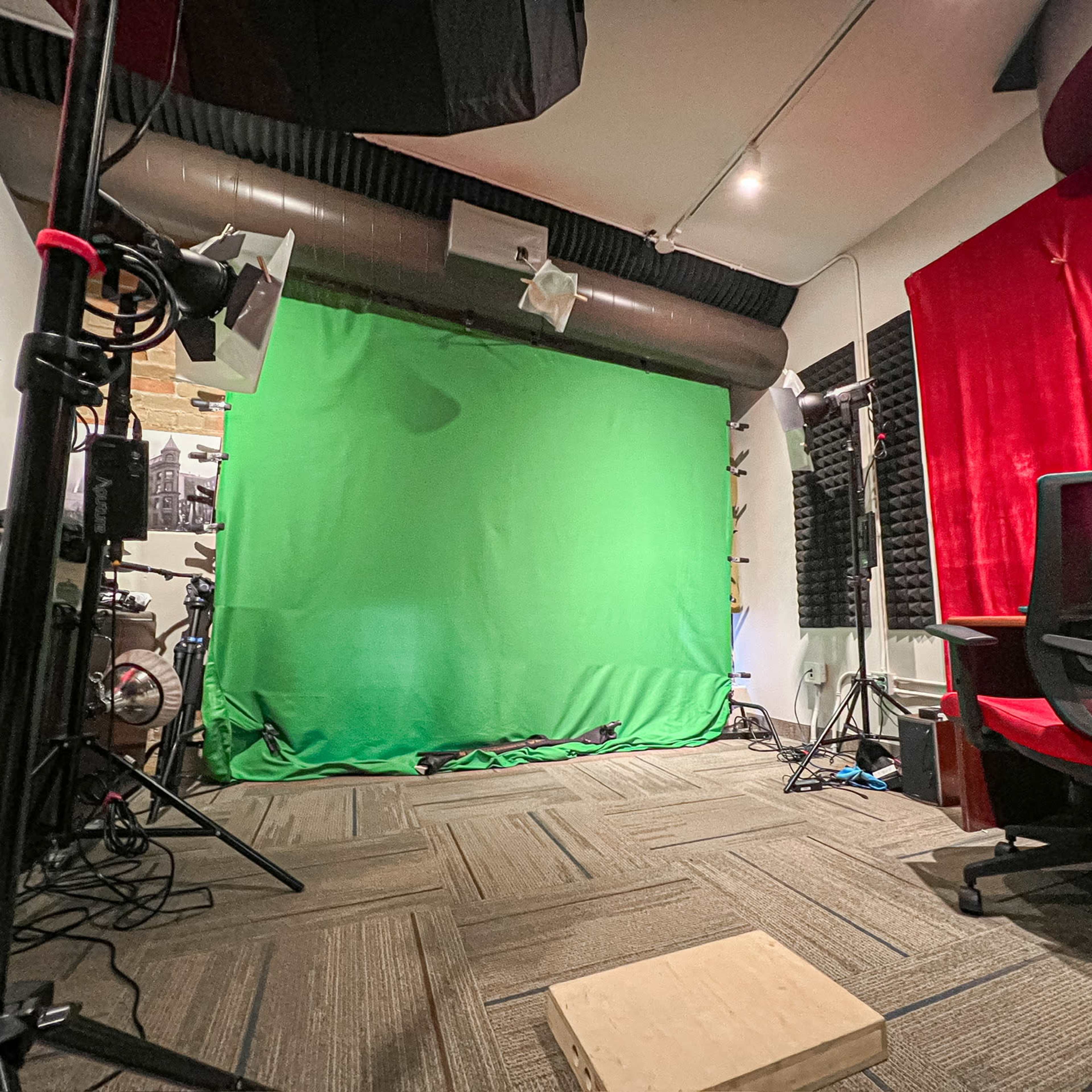 A studio setup featuring a green screen, lights, and a chair in a room with soundproofing panels.