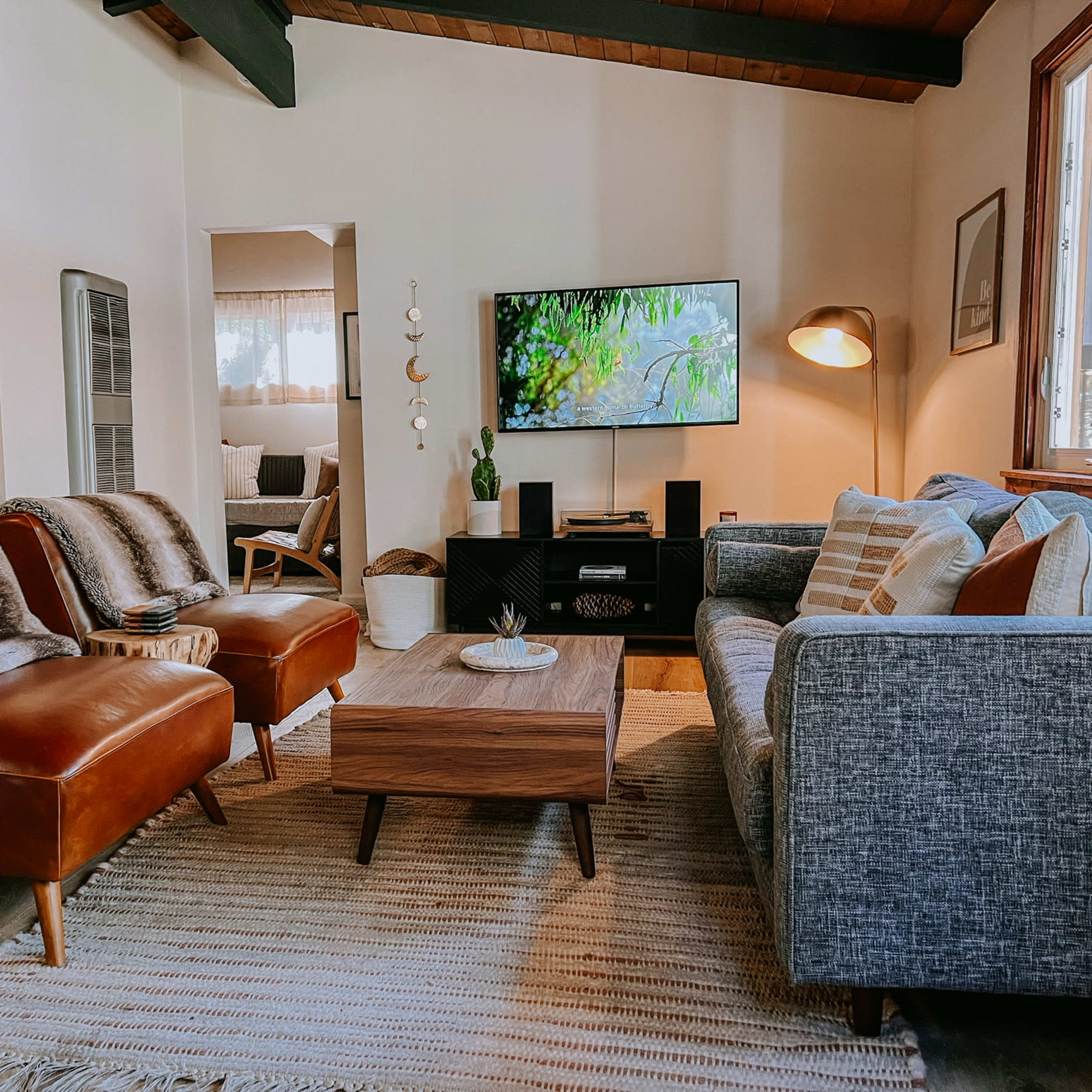 A cozy living room with two brown leather chairs, a gray sofa, a wooden coffee table, and a television displayed on the wall.