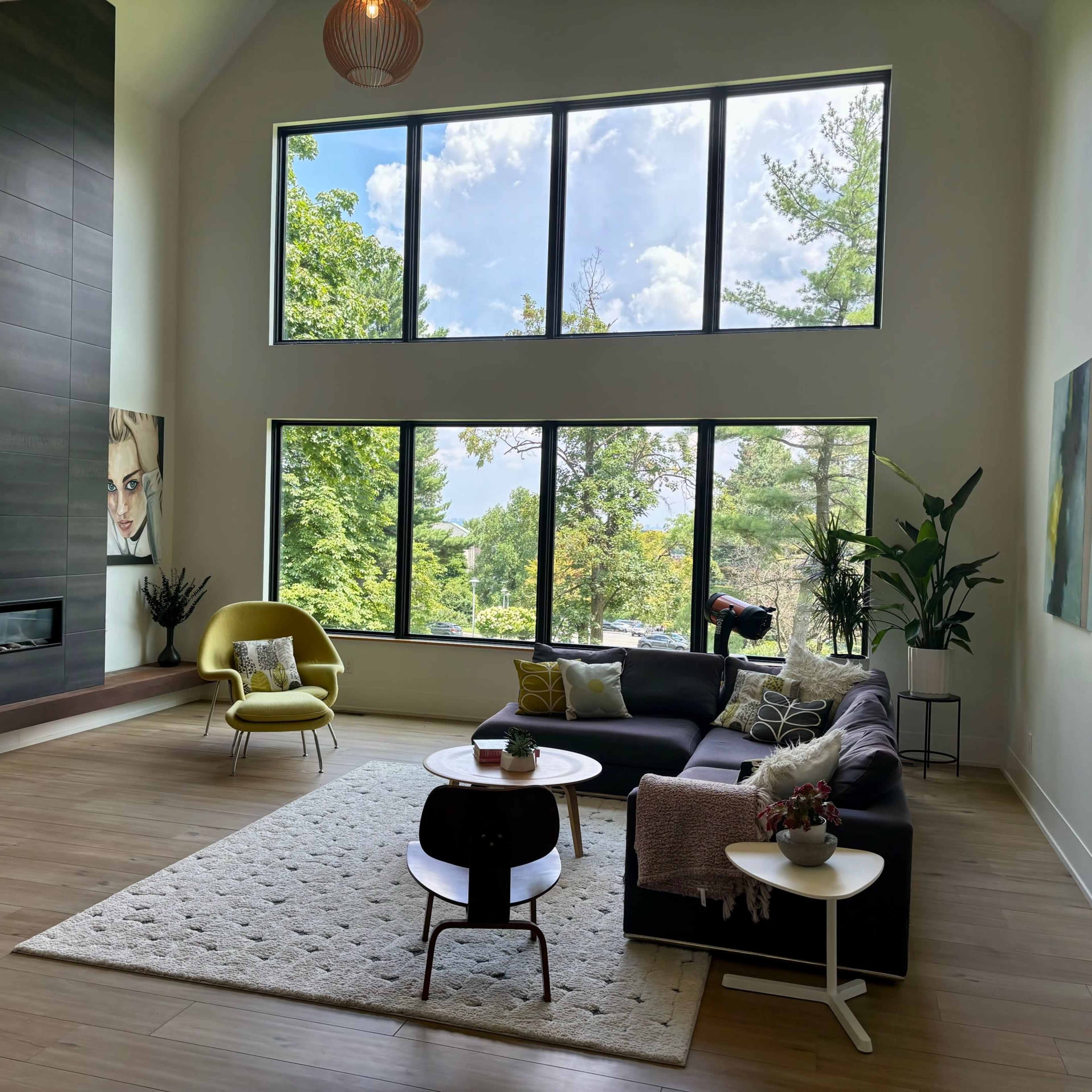 A modern living room with large windows, a sectional sofa, a yellow accent chair, and a coffee table on a light rug.
