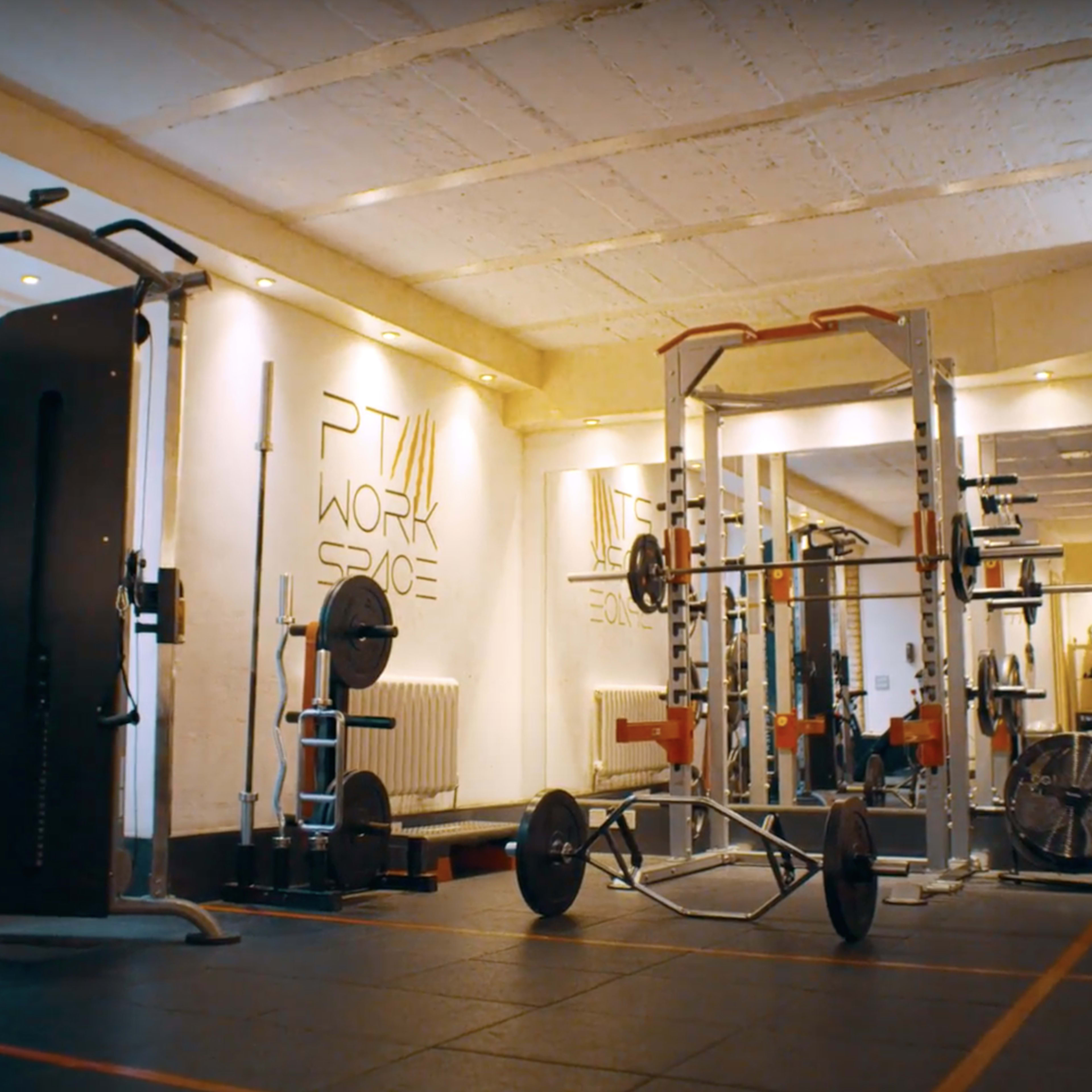 A gym interior equipped with various exercise machines and weights arranged on a black rubber floor.