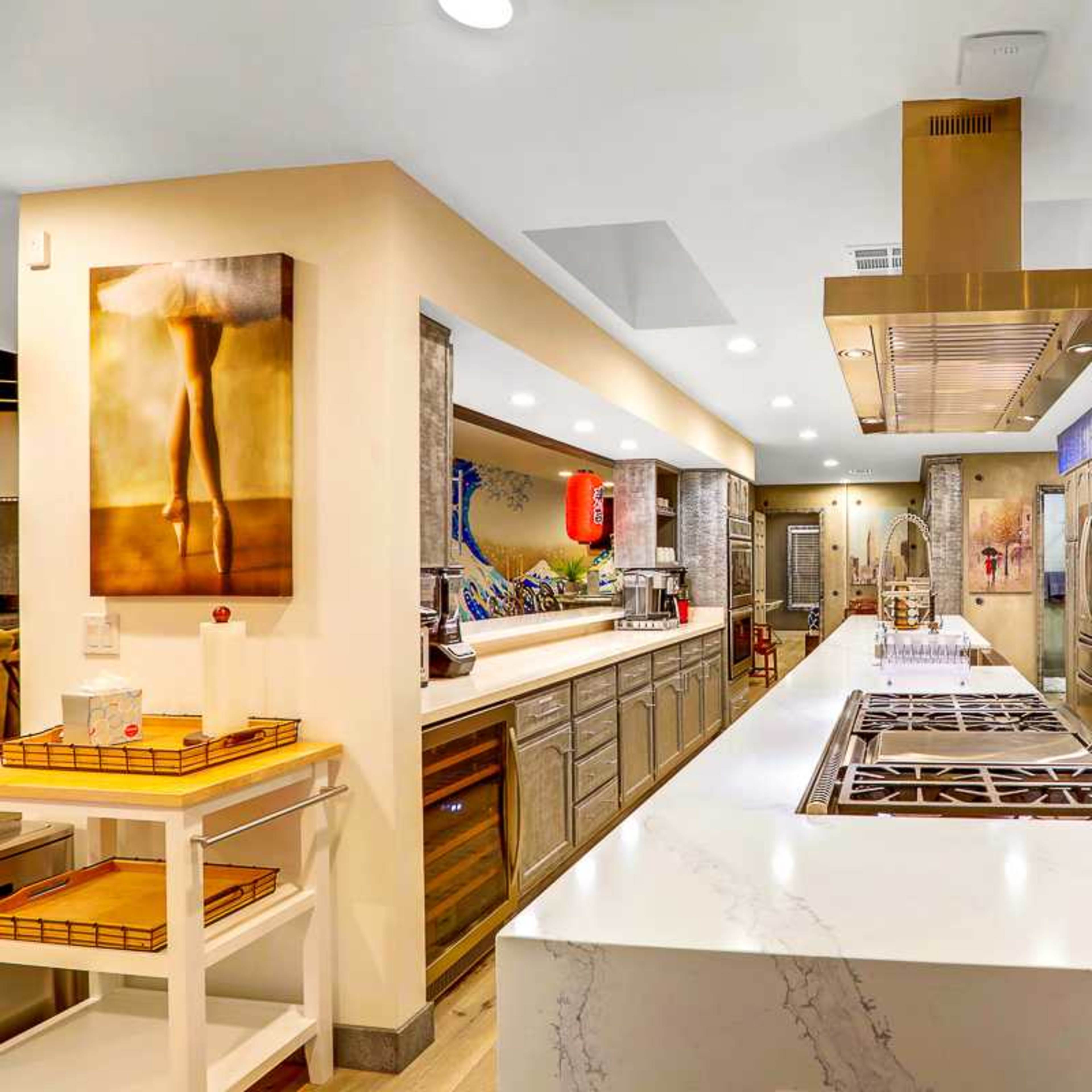The kitchen features a large central island with a stovetop, stainless steel appliances, and metallic cabinets against a blue backed wall.