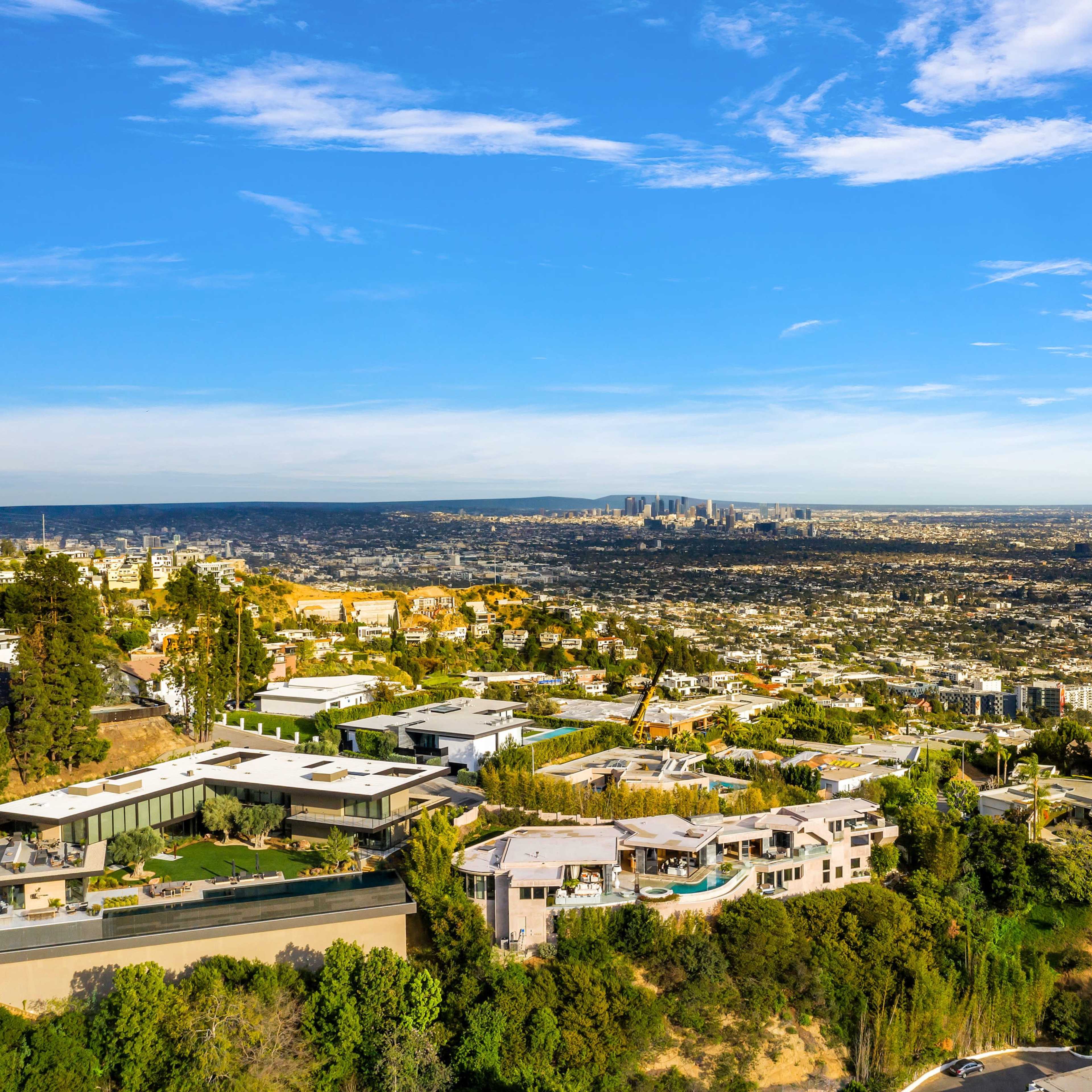 A sprawling hillside residential area with modern homes overlooking a cityscape under a clear blue sky.