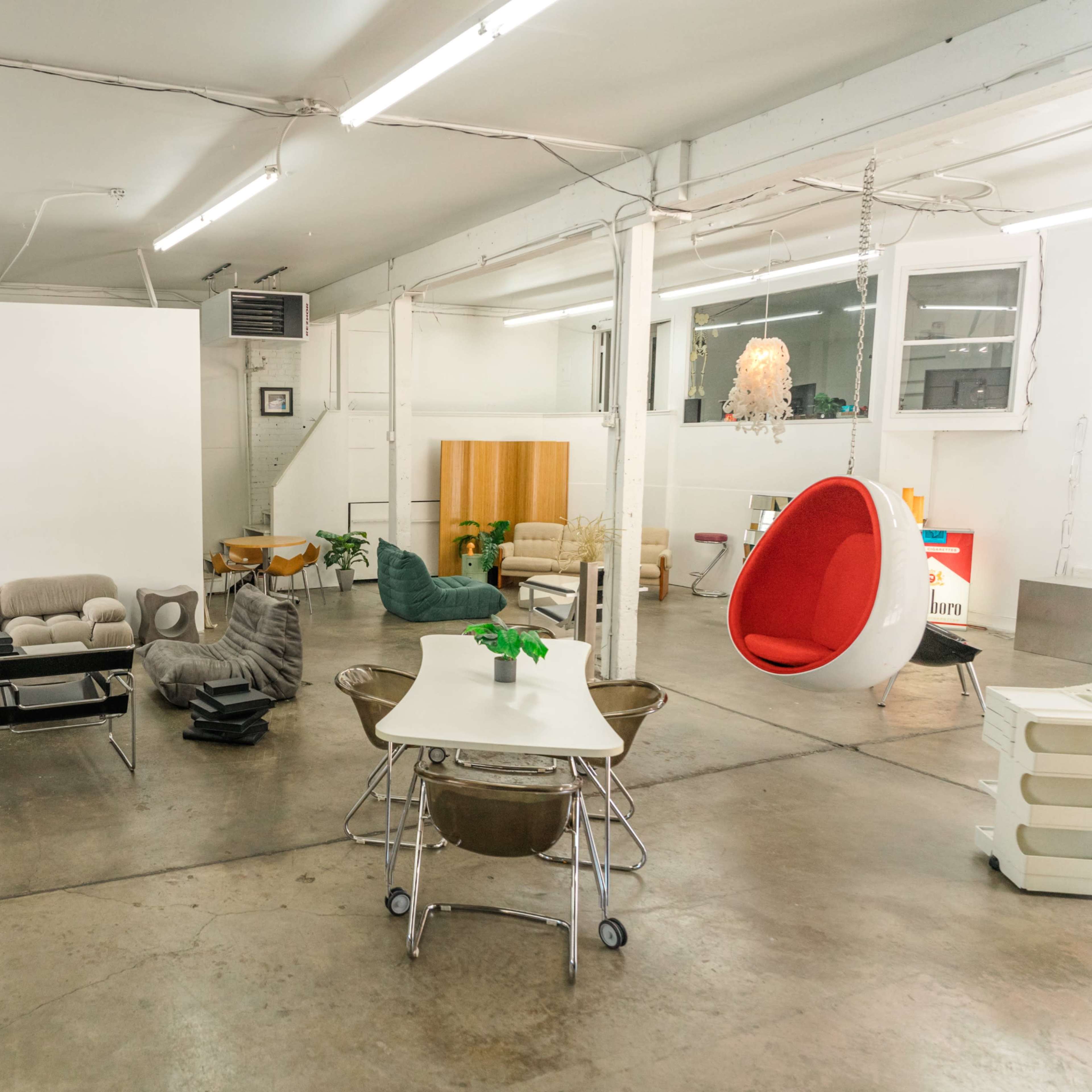 A spacious, minimalist interior filled with various modern furniture pieces, including couches, a hanging chair, and a dining table.