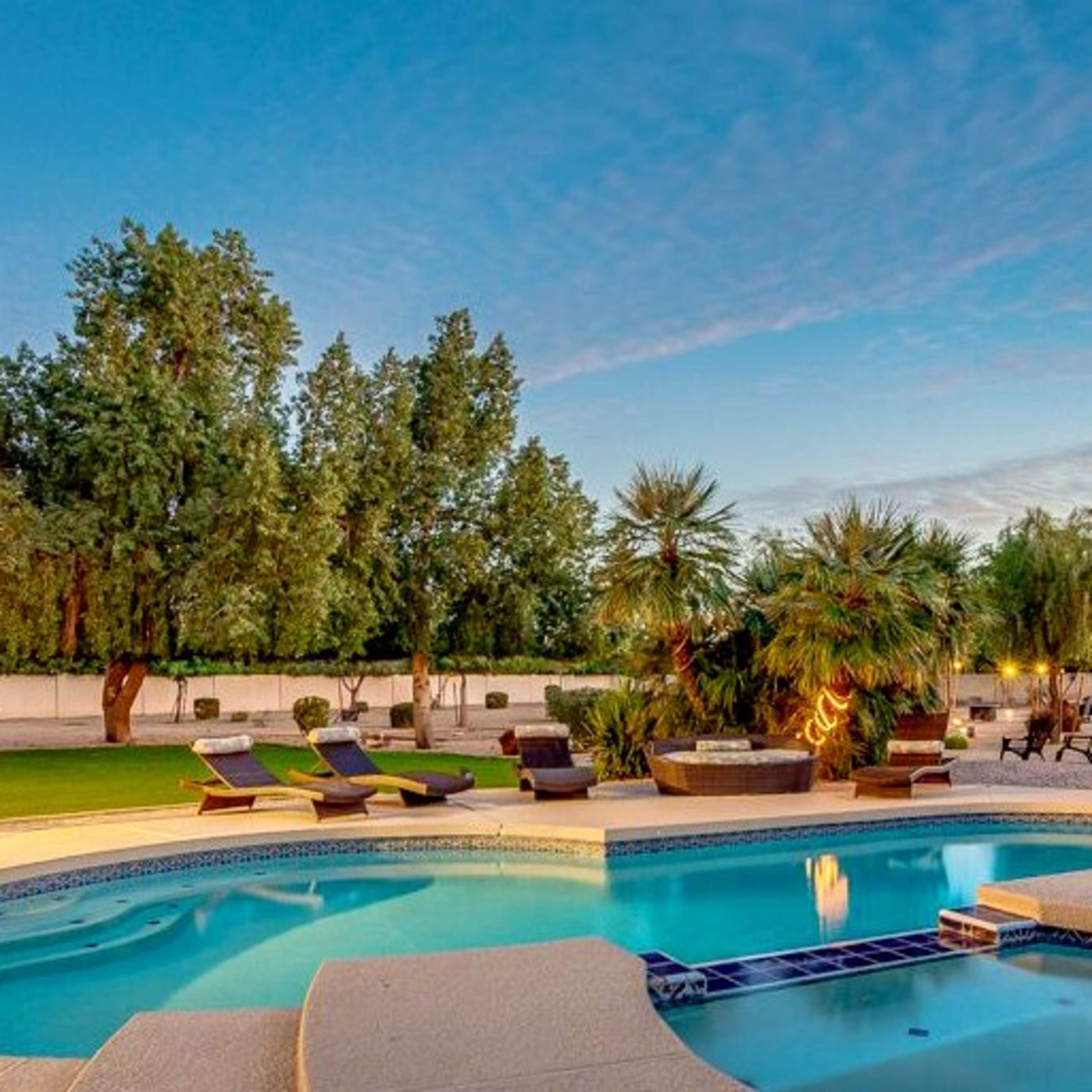 A swimming pool surrounded by lounge chairs and palm trees in a spacious backyard.