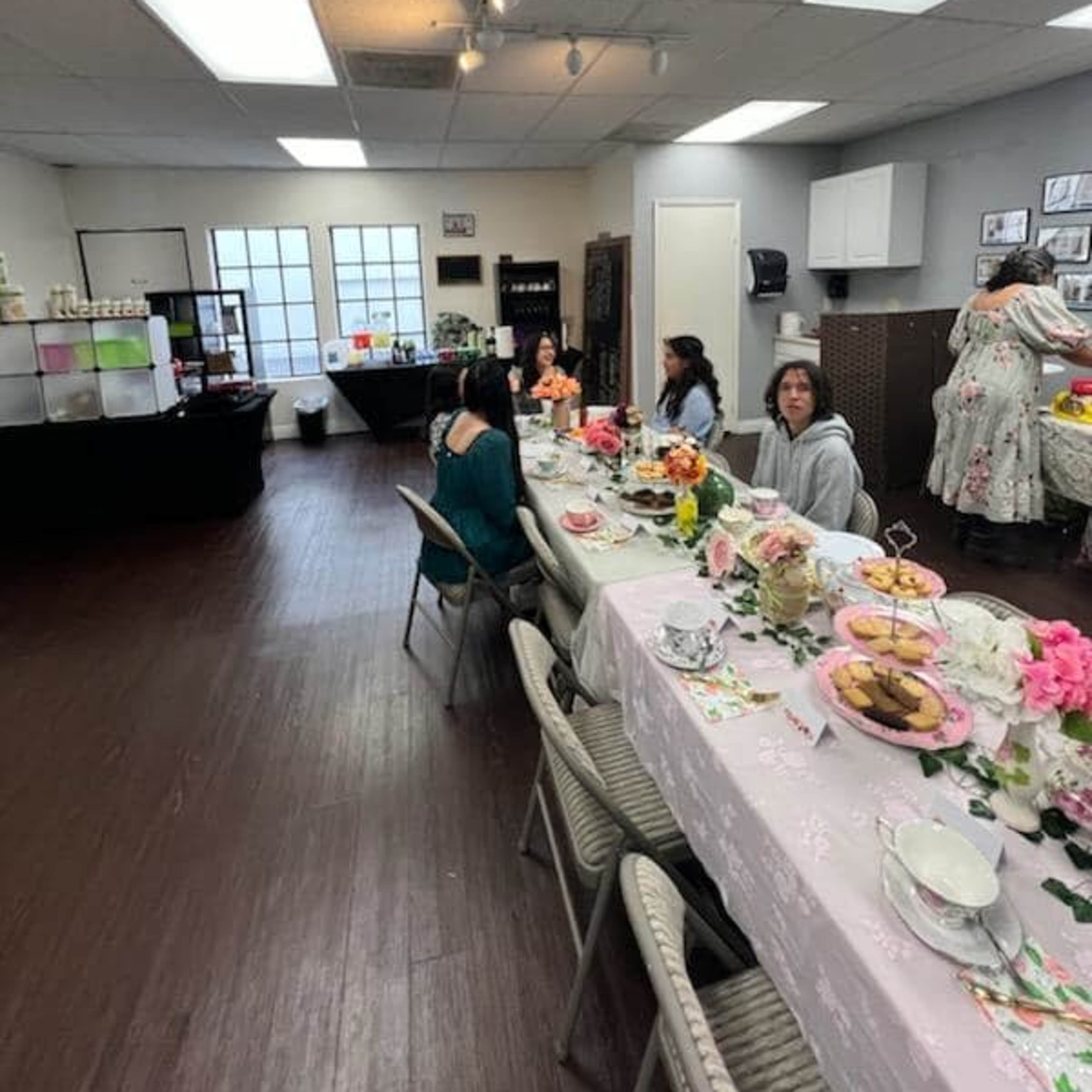 A group of people sits at a long, table covered with food and decorations in a well-lit room.
