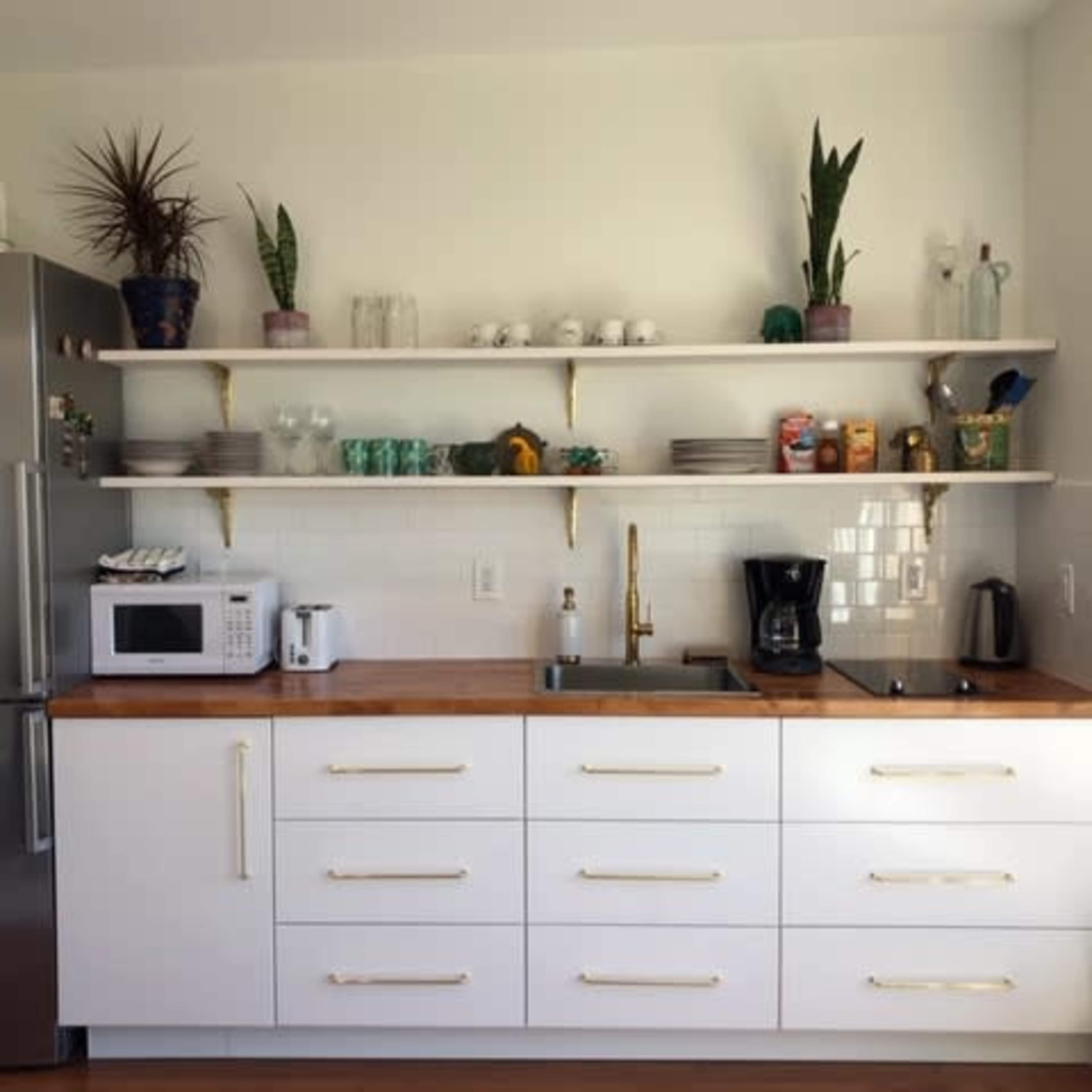 A modern kitchen features a stainless steel refrigerator, white cabinets, wooden countertops, and open shelving displaying various kitchen items and plants.