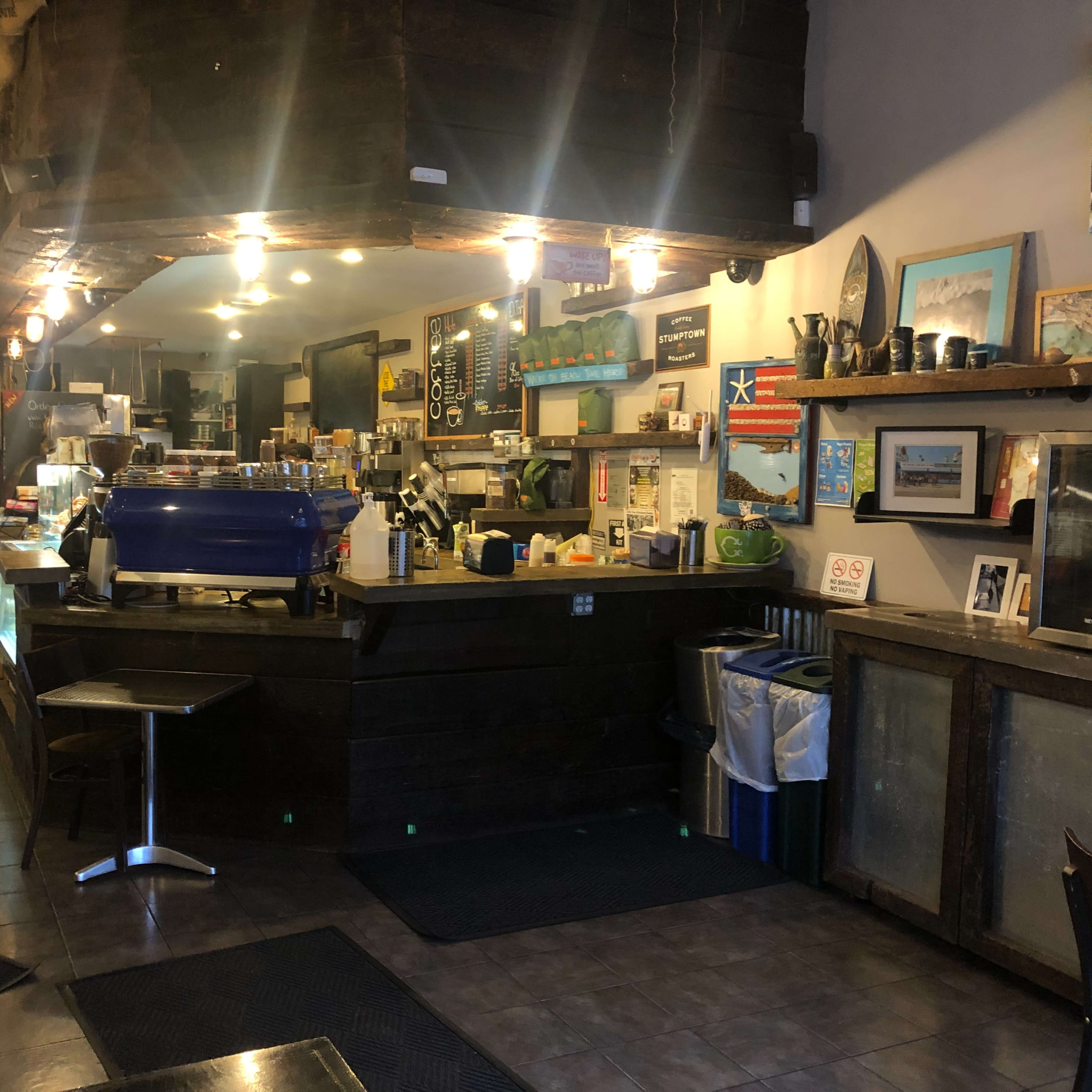 A cozy café interior with a wooden counter, a blue espresso machine, and seating areas.