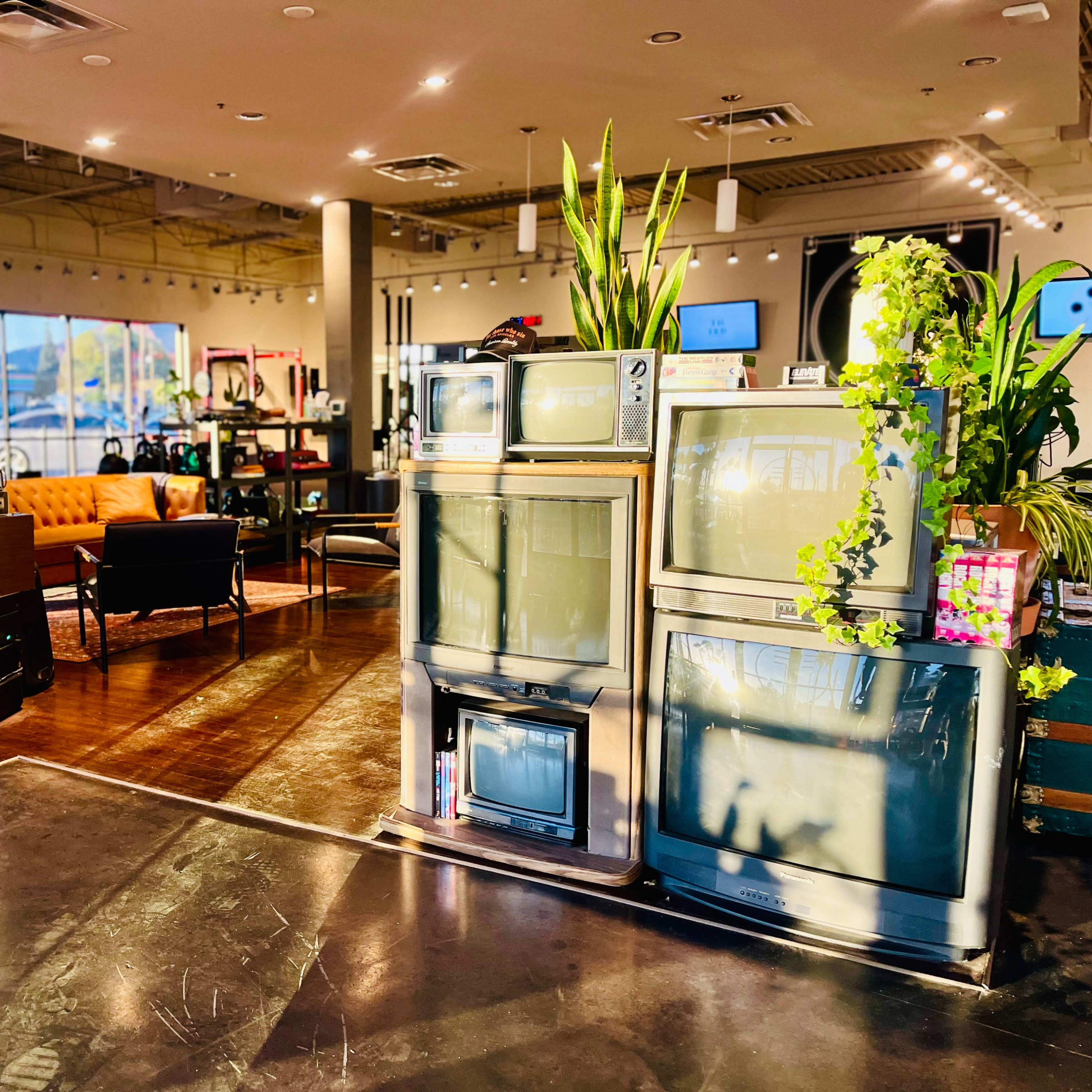 The interior of a vintage store features several retro televisions displayed alongside modern furniture and potted plants.