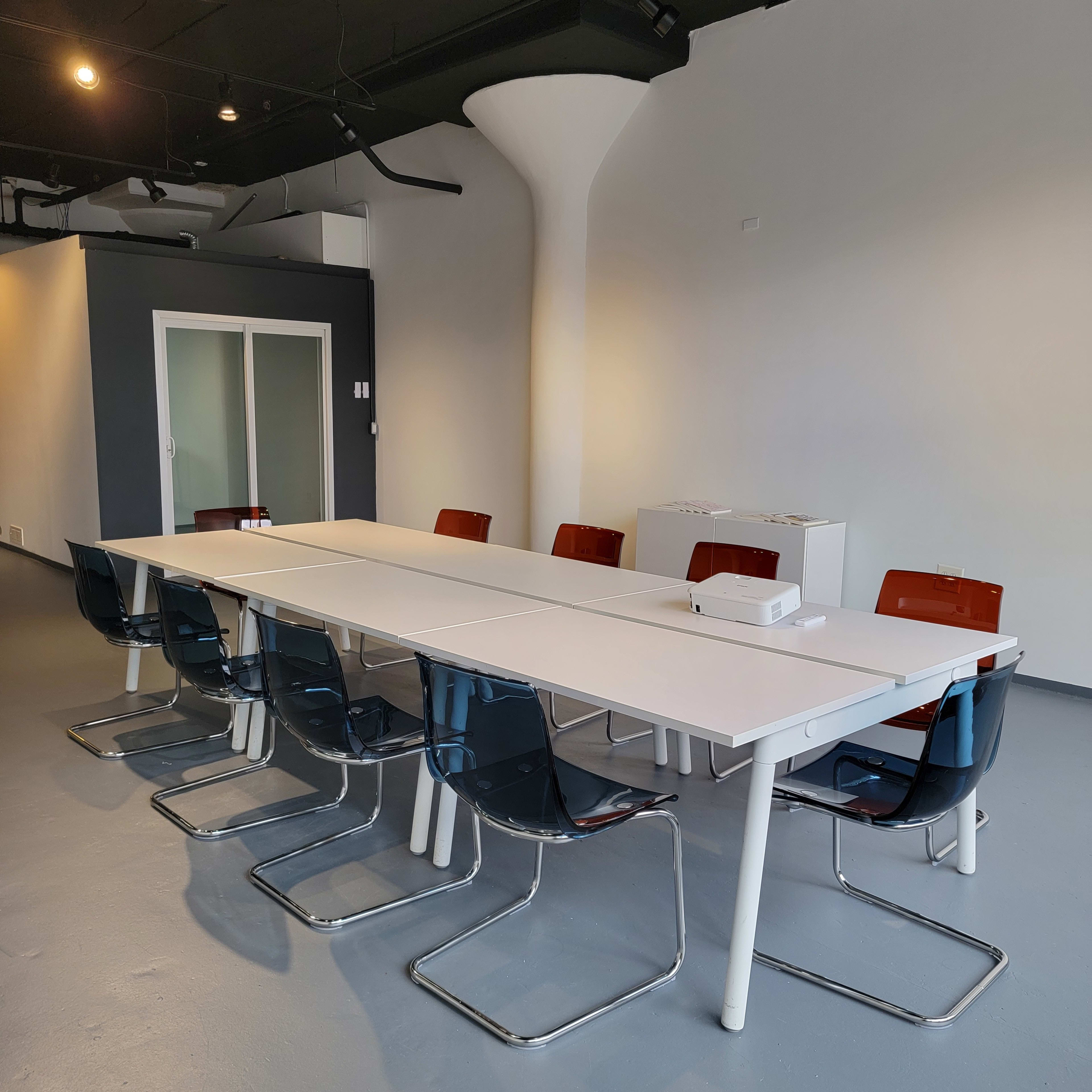 A large, modern conference table is surrounded by transparent chairs in a minimalistic room with a gray floor and white walls.
